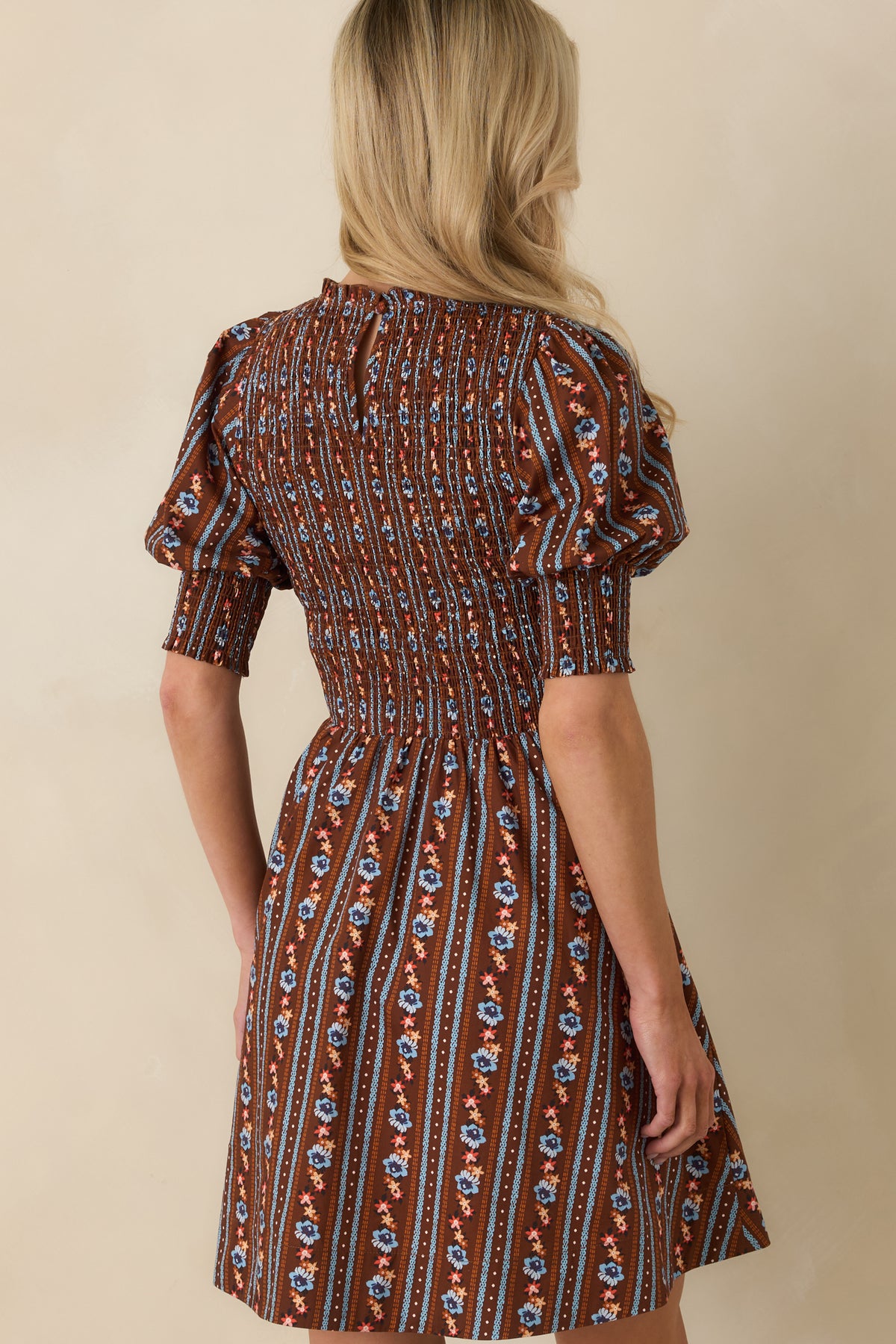 Rear view of the floral mini dress featuring extensive bodice smocking, wide smocked cuffs, and a back keyhole closure.