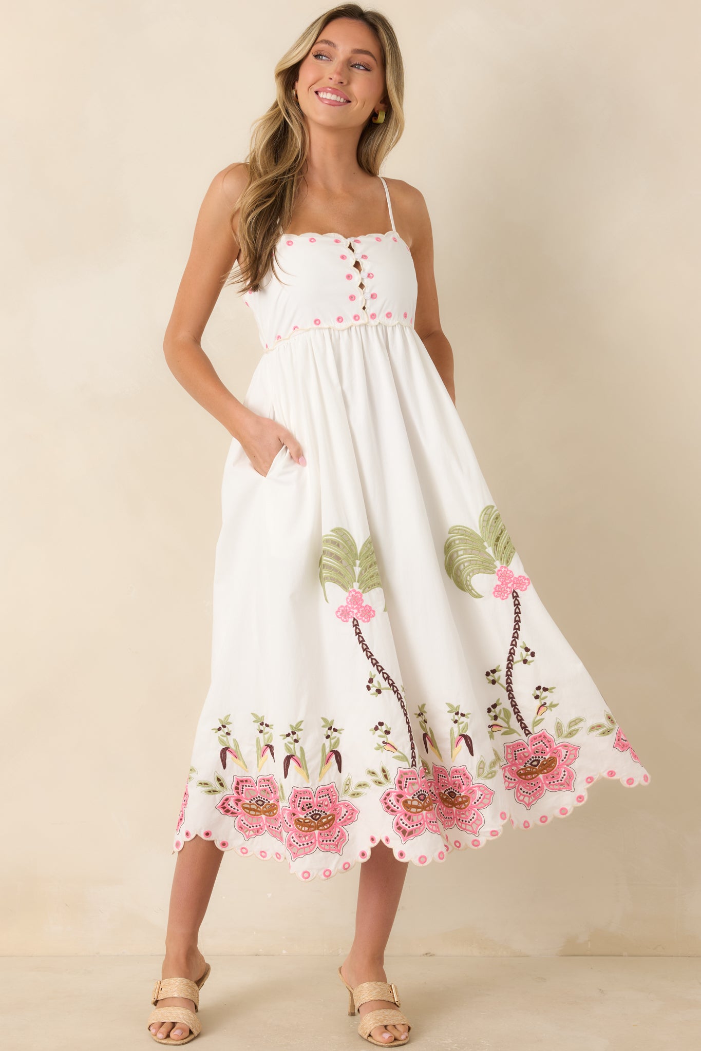 Feminine midi dress showcasing a scalloped neckline, adjustable straps, smocked back design, and a floral palm tree embroidered hem.
