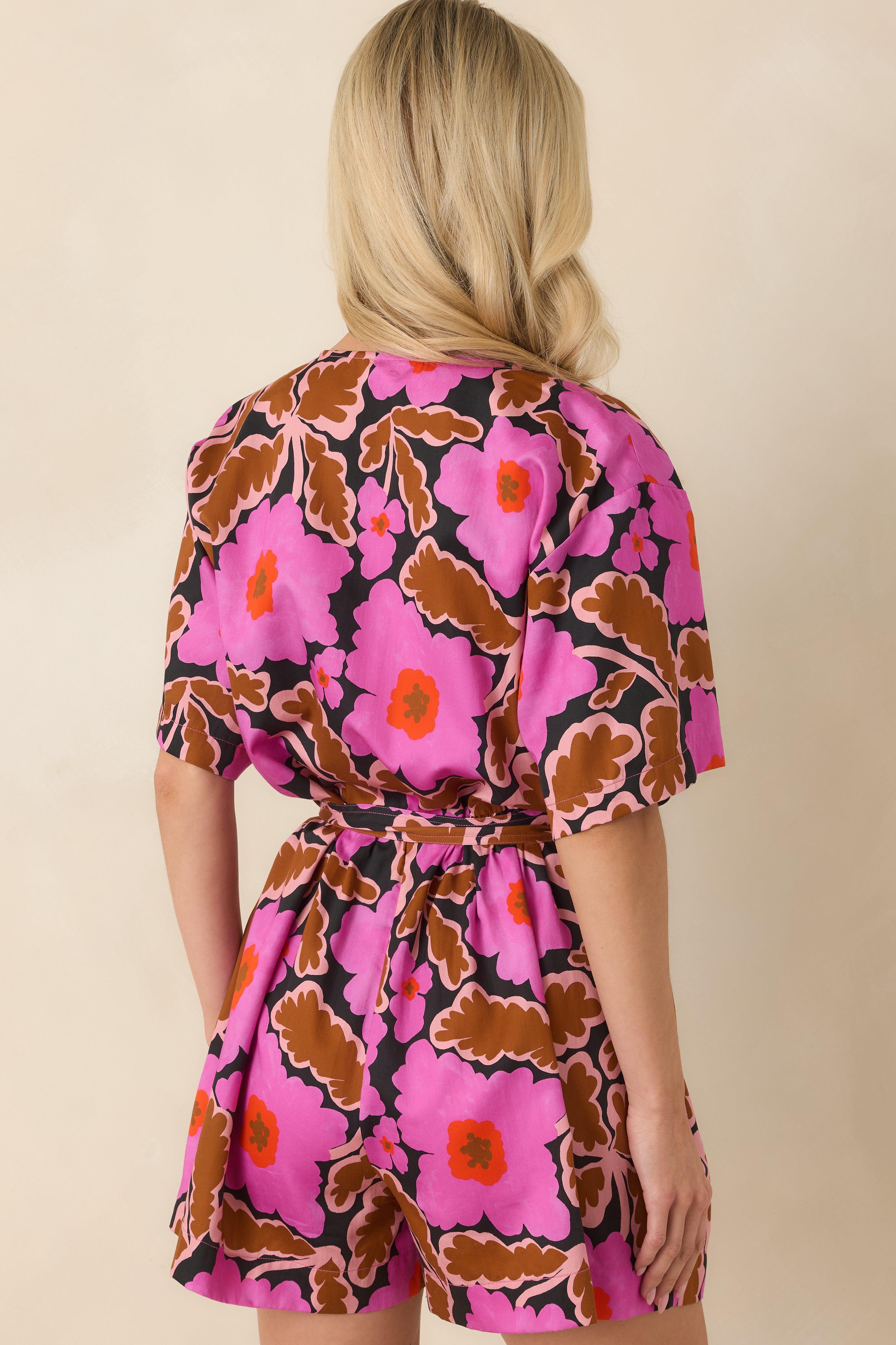 Rear view of the floral romper featuring a relaxed silhouette, short sleeves, tied waist, and breezy shorts.