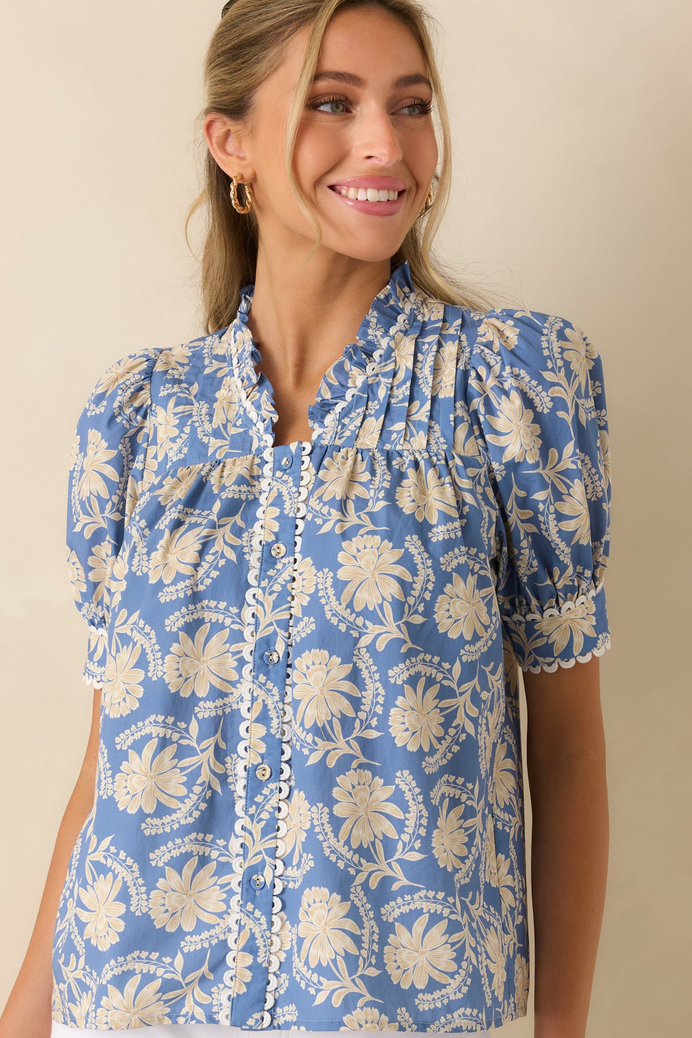 Close view of the floral blouse highlighting the ruffled stand collar, button-front placket, and scalloped trim detailing.