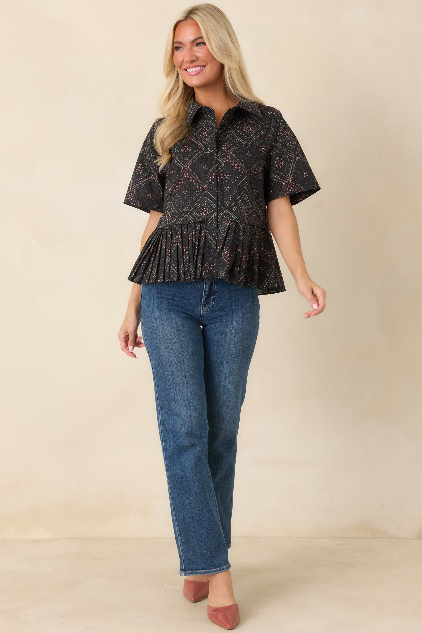 Cotton blouse with a black backdrop showcasing coral and green floral motifs in a geometric scarf print, finished with a classic collar, button front, and pleated peplum silhouette.