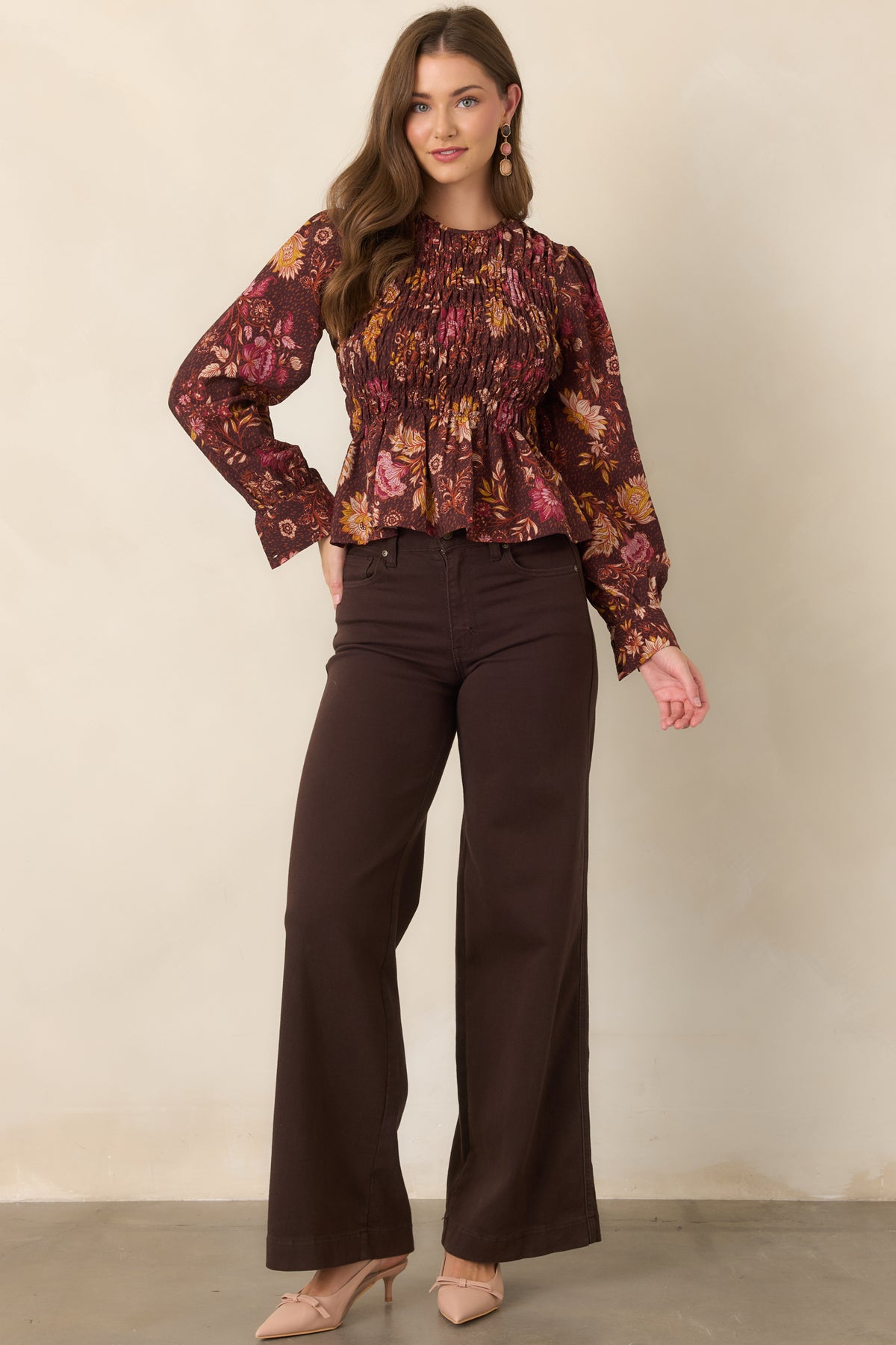 Floral peplum top featuring a chocolate brown background, colorful pink and golden yellow blooms, stretchy smocking through the bodice, and voluminous puff sleeves with button cuffs.