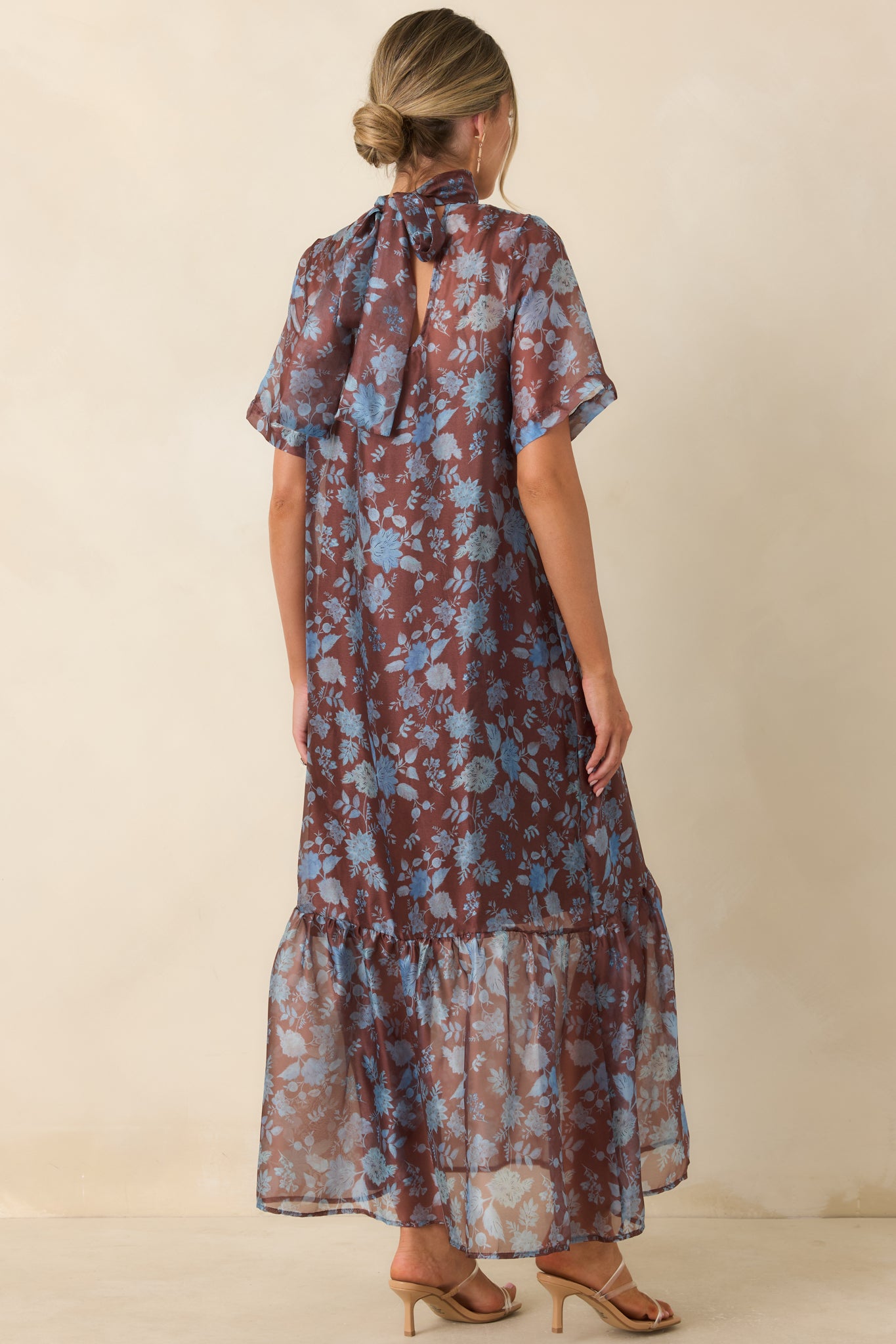 Rear view of the floral maxi dress featuring the tied mock neckline, flowing overlay, and layered maxi silhouette.