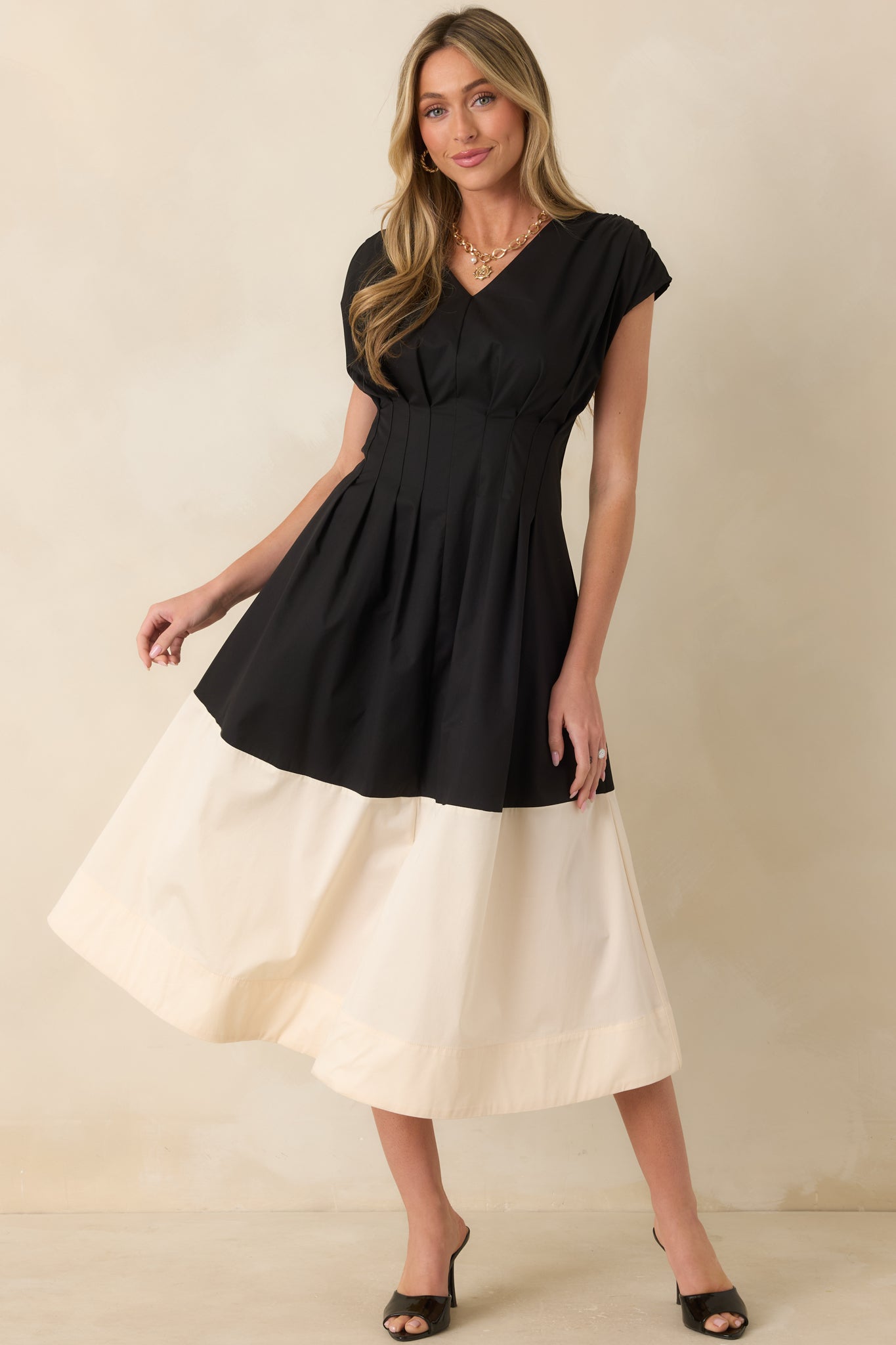 Flowing black and ivory midi dress featuring a structured pleated bodice, V-neckline, and practical side pockets.