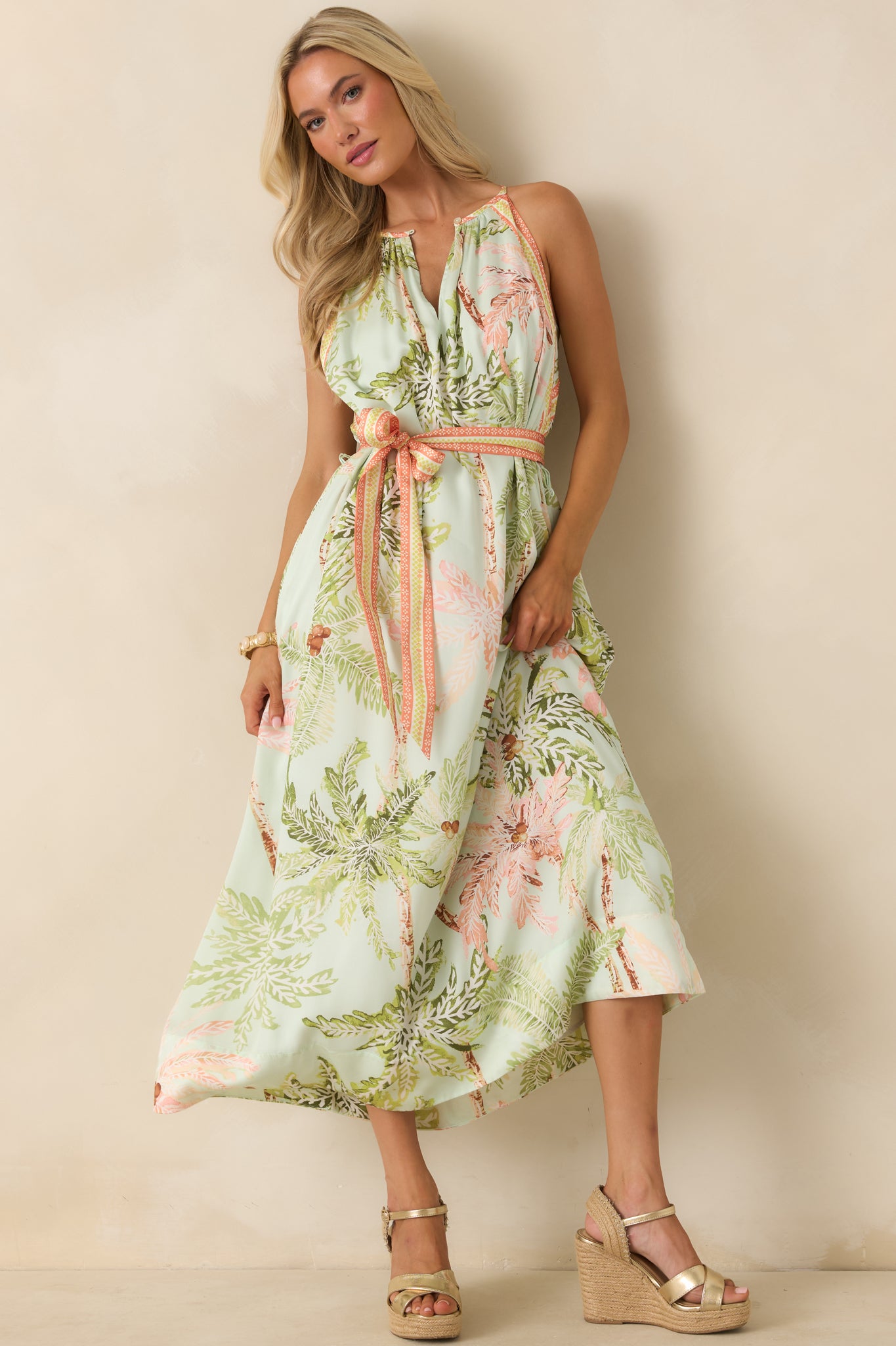 Flowing resort-style maxi dress with a sleeveless cut, subtle front keyhole, and an allover palm print blending blush, green, and warm earthy hues.