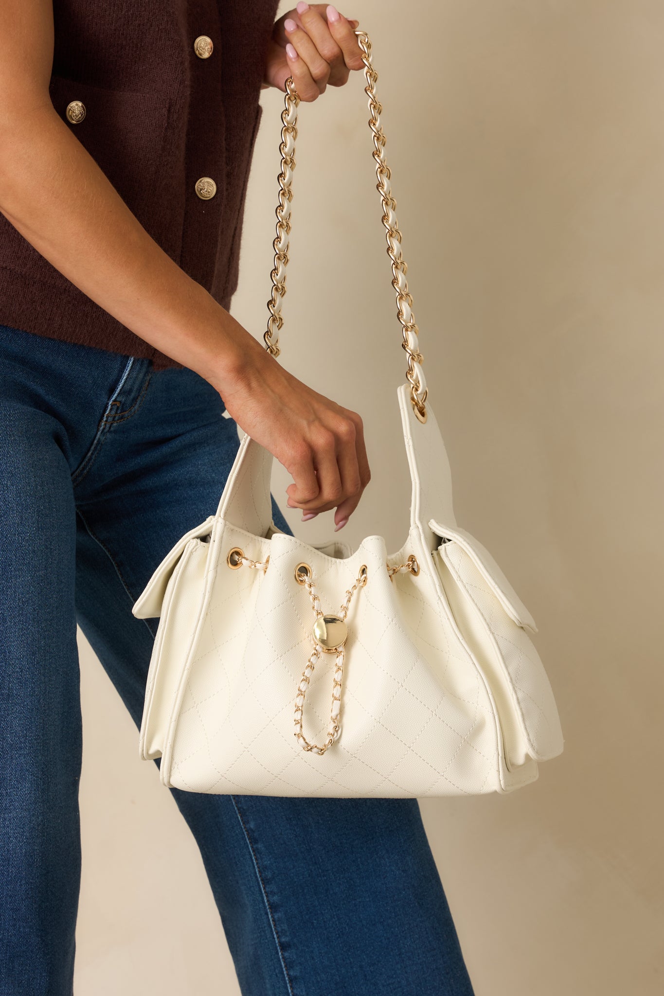 Focus on fold-over side pocket and interlaced gold chain strap on white quilted purse.