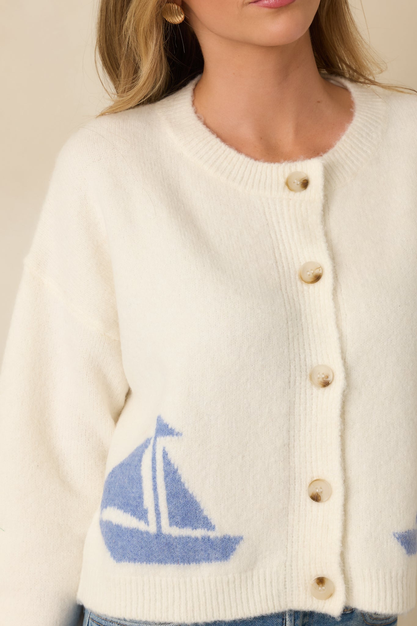 Focused close-up of sailboat knit design and button closure on ivory lightweight cardigan.