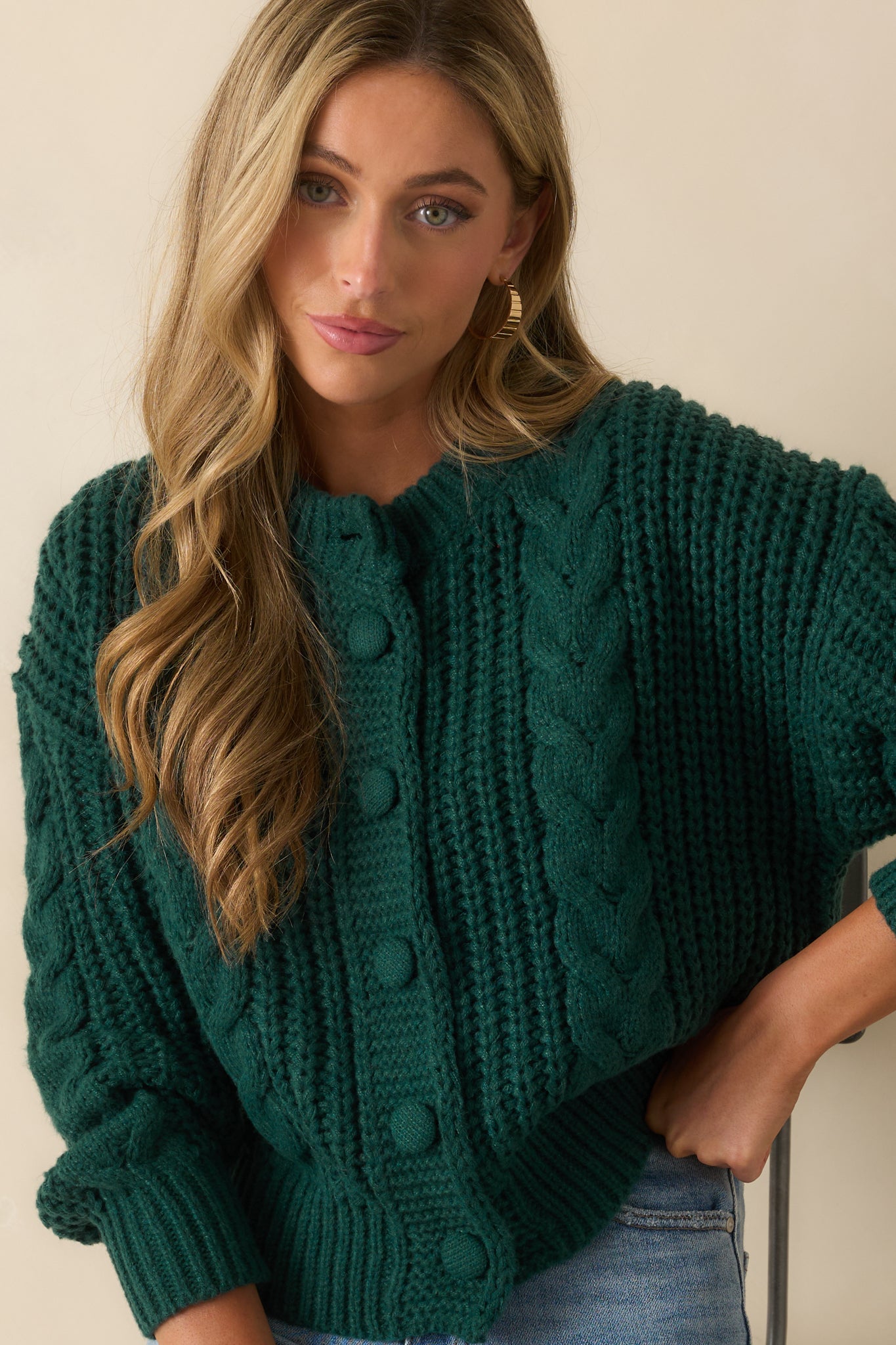 Close view of the ribbed crew neckline and textured cable knit on the forest green cardigan.