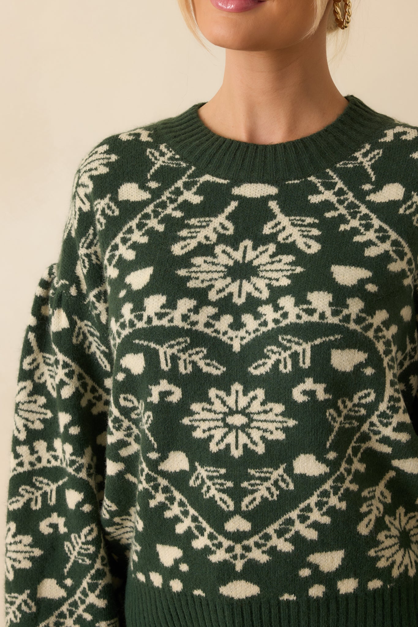 Detailed shot of the forest green sweater showcasing the heart-patterned knit, ribbed crew neckline, and balloon sleeve cuffs.