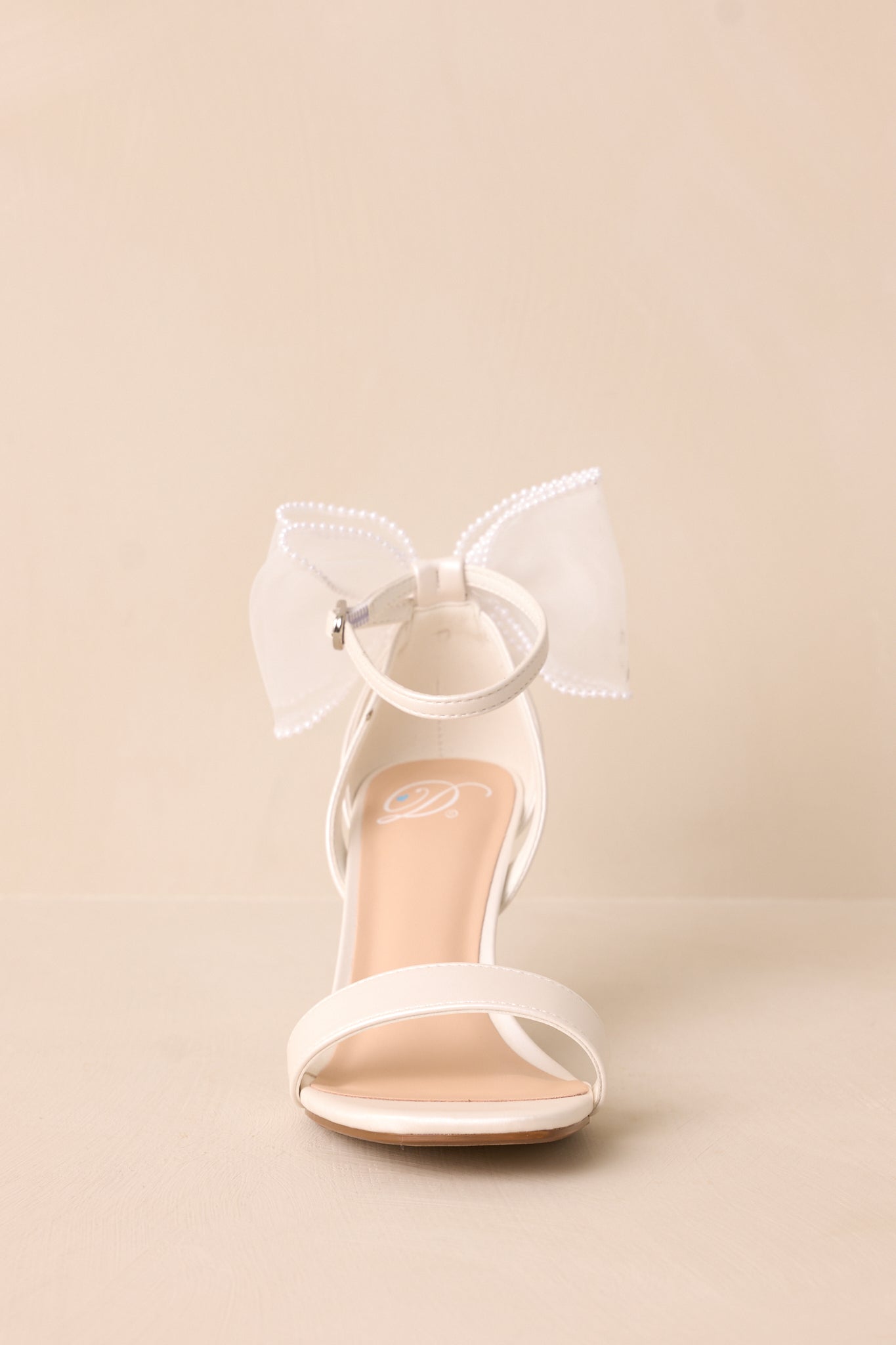 Front angle of the white heels, focusing on the toe strap and ankle strap with silver buckle, with the lace bow delicately positioned at the back.