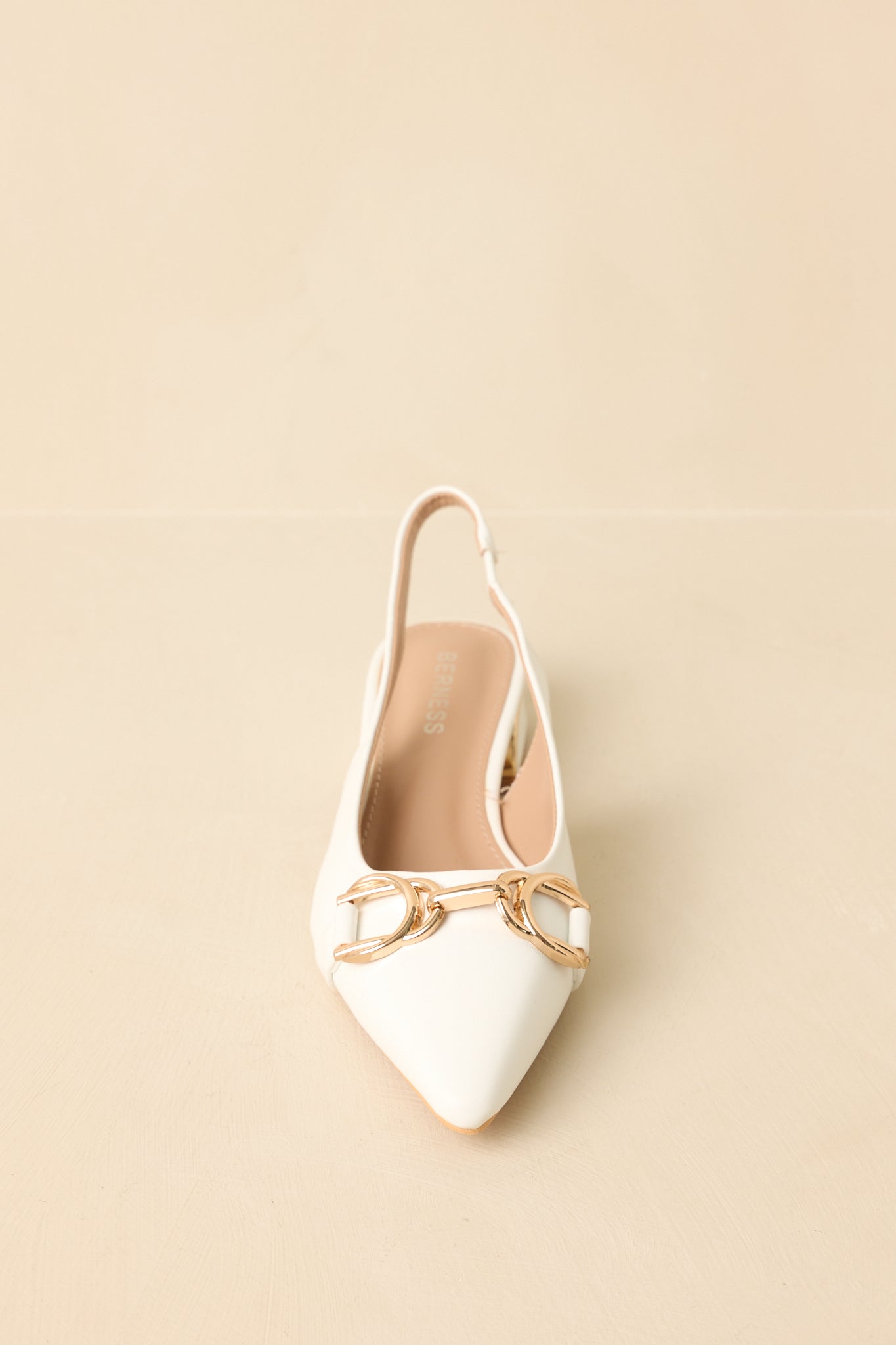 Front-facing view of white pointed-toe slingback flats against a beige background highlighting the gold hardware detail.