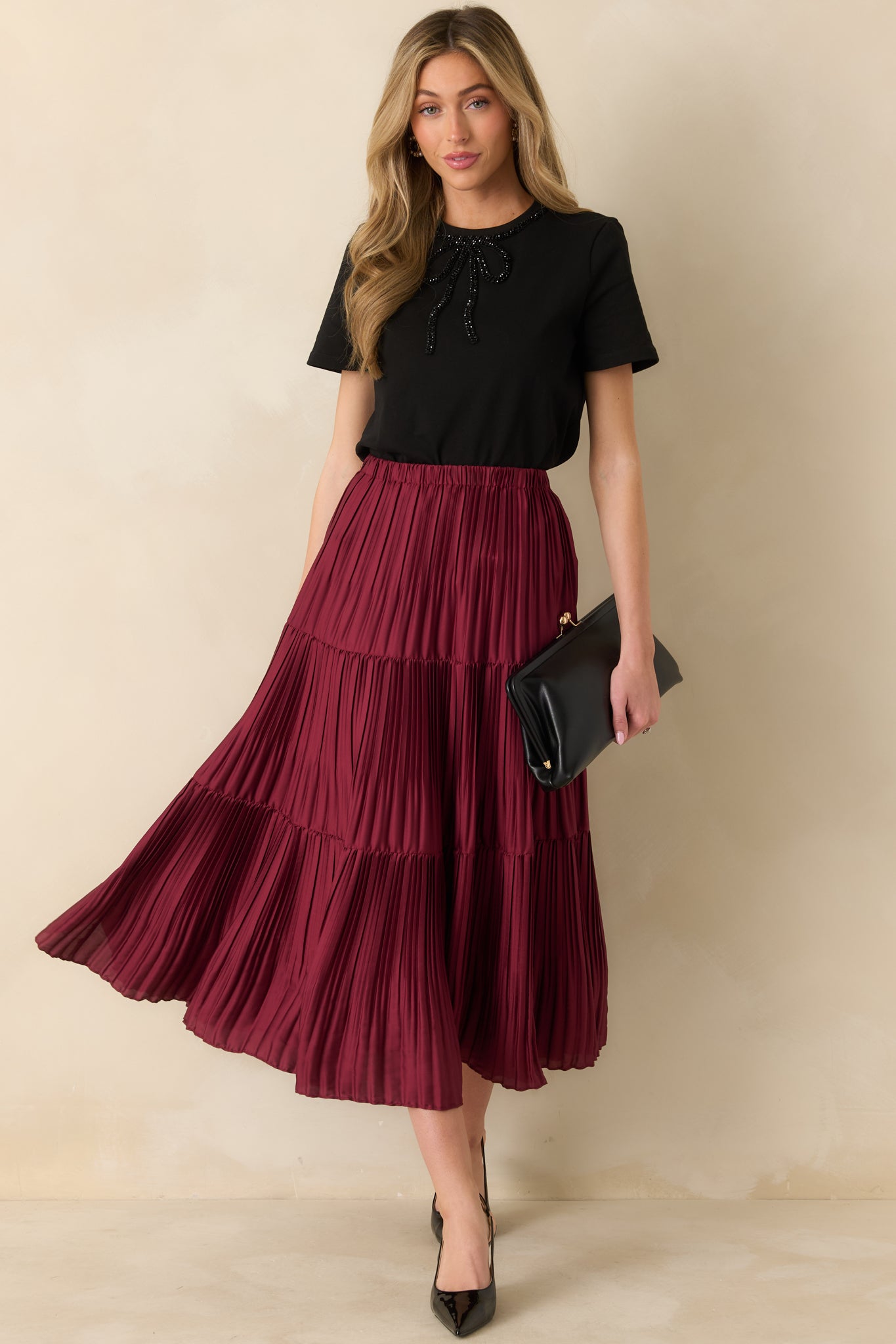 Front view of burgundy tiered pleated midi skirt with flowy A-line silhouette and elastic waistband.