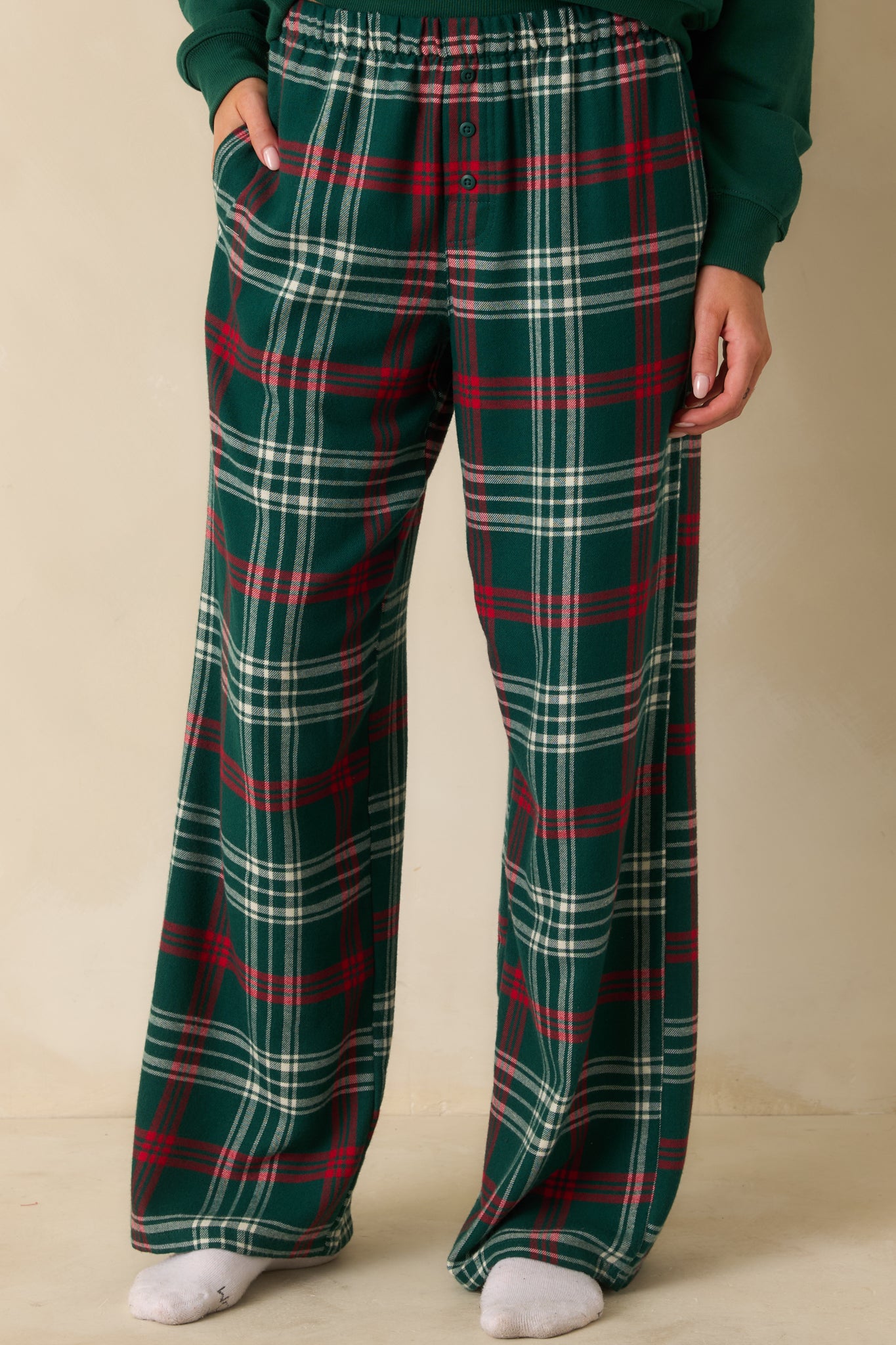 Detail of front of green pajama pants, emphasizing elastic waistband, side pockets, and plaid pattern.