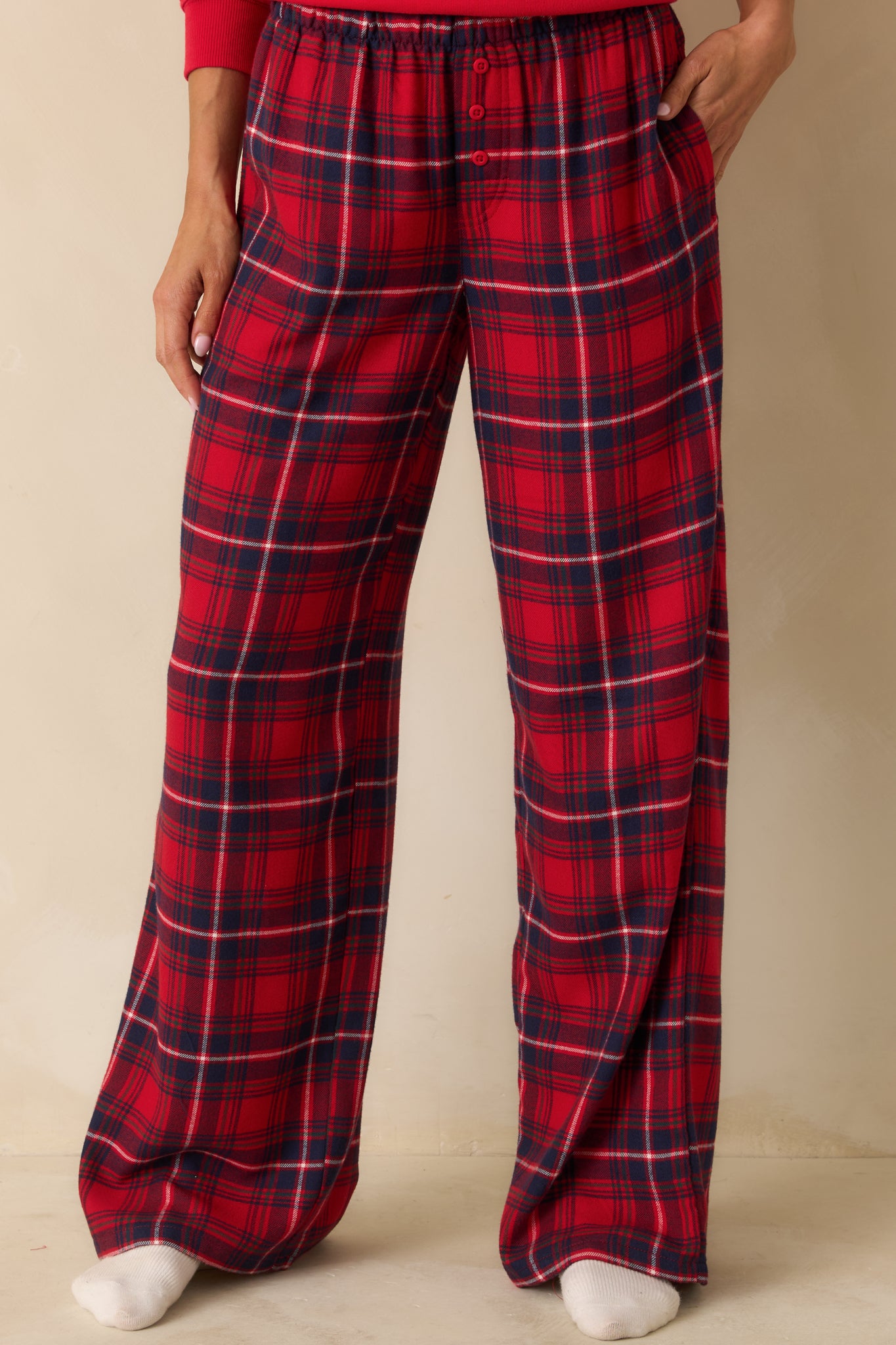 Detail of front of red pajama pants, emphasizing elastic waistband, side pockets, and plaid pattern.