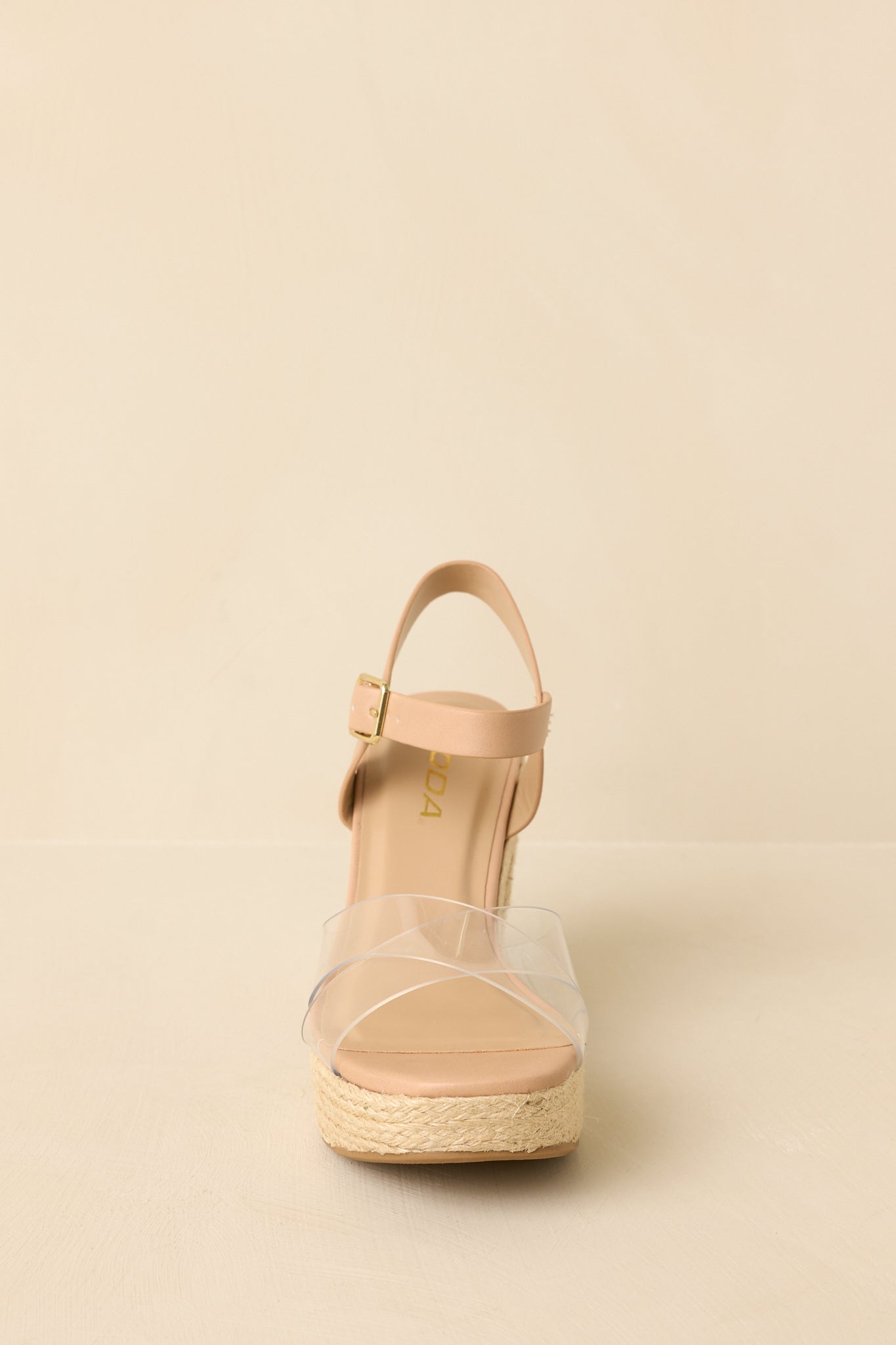 Front-facing view of natural raffia platform sandals against a beige background highlighting the clear vamp strap.