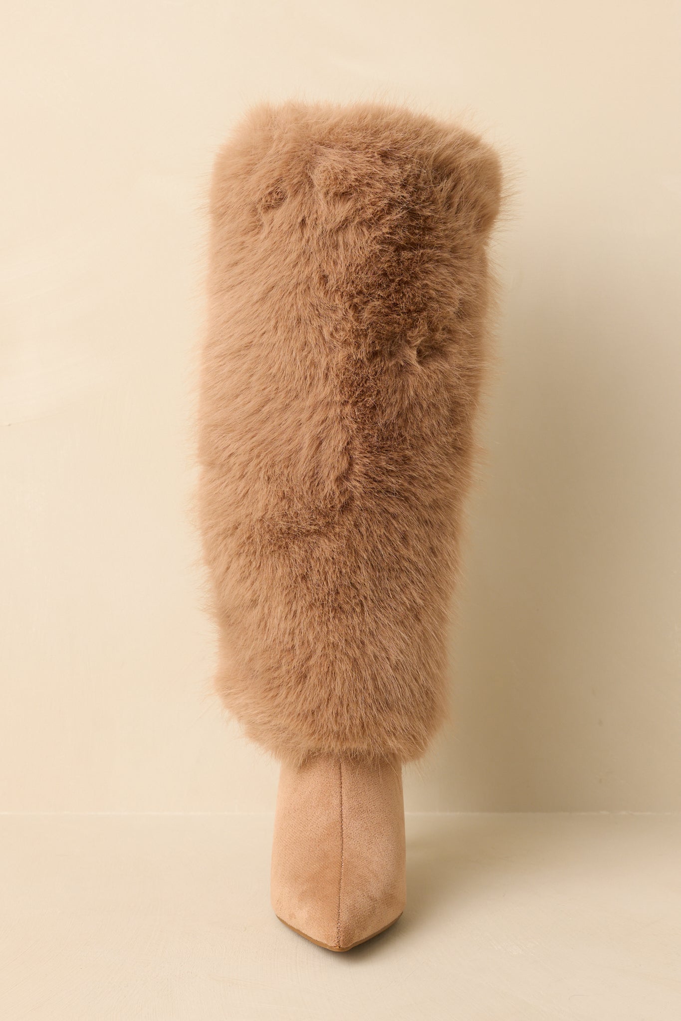 Front-facing view of tan knee-high stiletto boots against a beige background highlighting the pointed toe and slim heel.