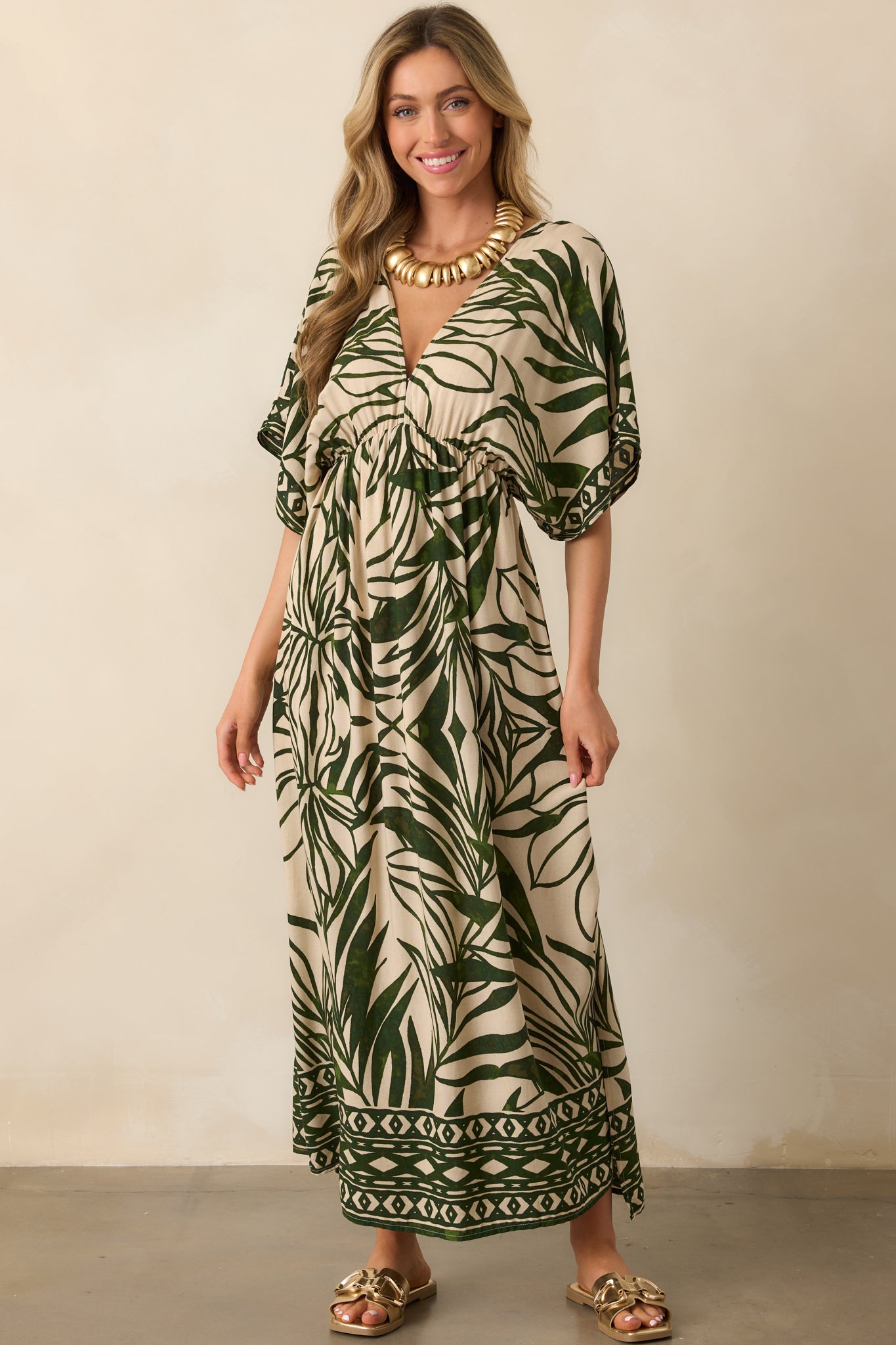 Front-facing view of a palm leaf print maxi dress in green and beige, highlighting the geometric hemline pattern, kimono sleeves, and deep V-neck.