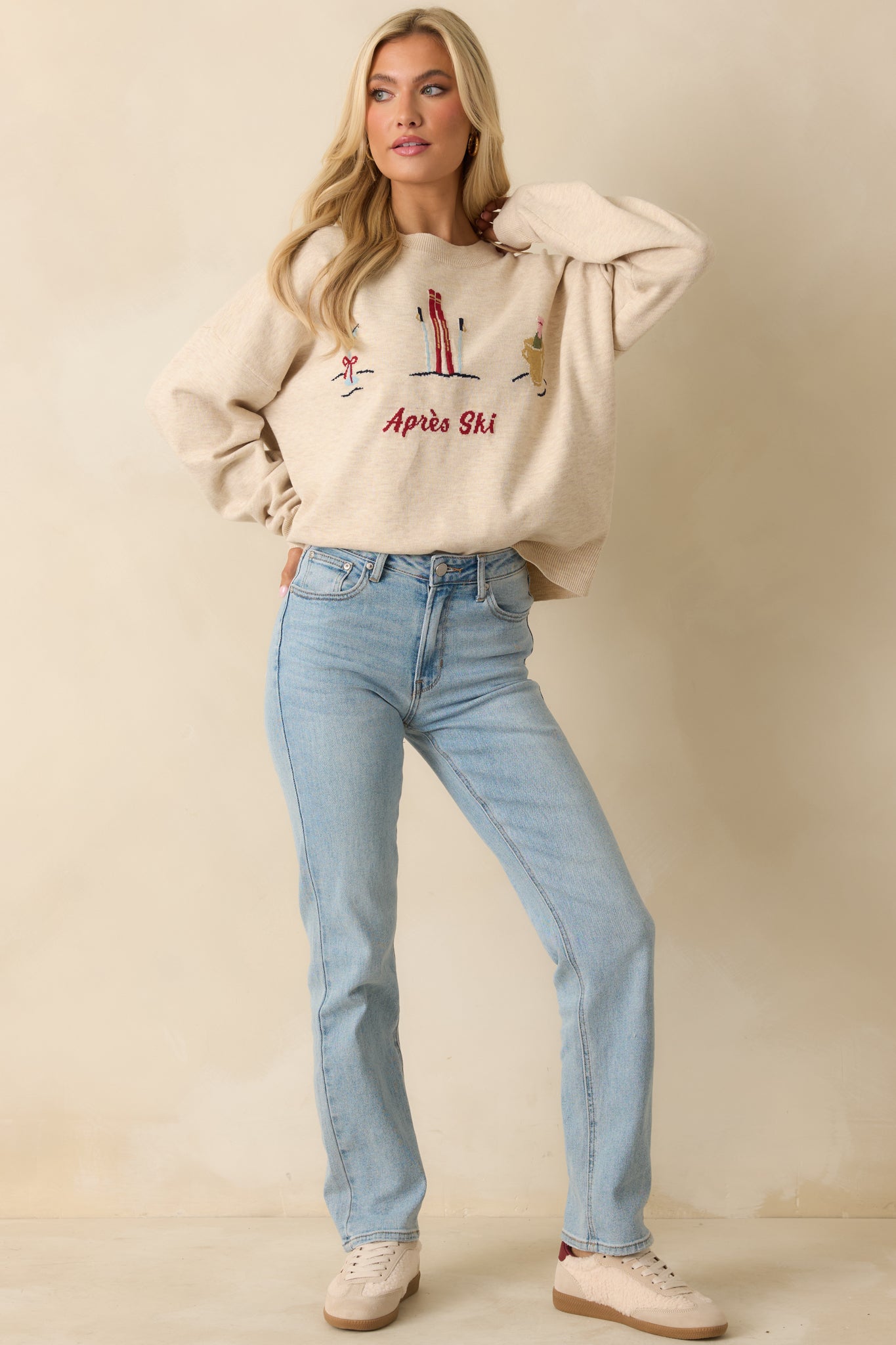 Front view of the heathered oatmeal crewneck sweater showing long sleeves, ribbed neckline and cuffs, and the embroidered ski and cocktail motifs with “Après Ski” script.
