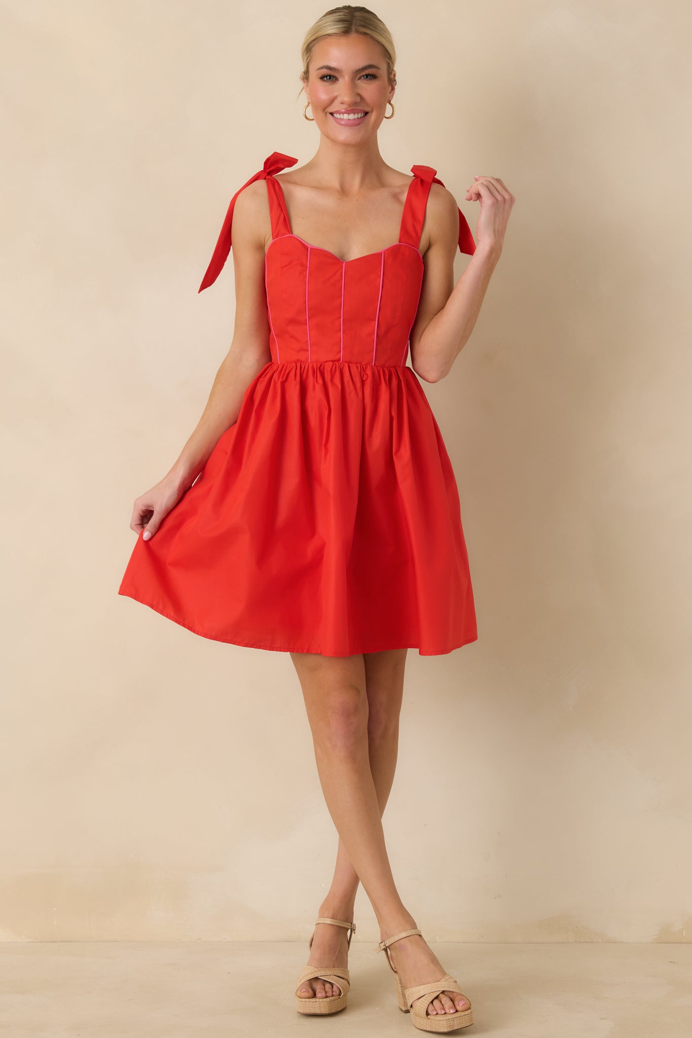 Front view of a red mini dress with a sweetheart neckline, corset-style pink trim on the bodice, and adjustable self-tie bow straps.