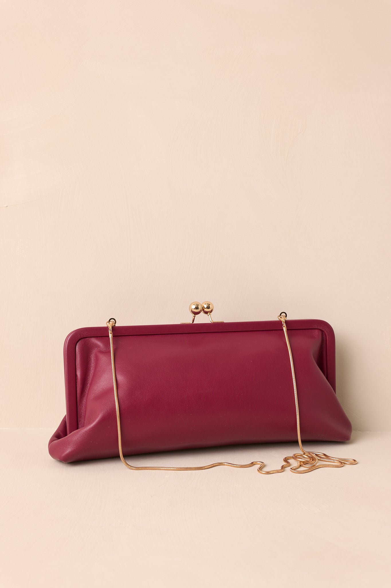 Front view of the burgundy faux leather clutch showing its structured frame silhouette and gold-tone kiss-lock closure.