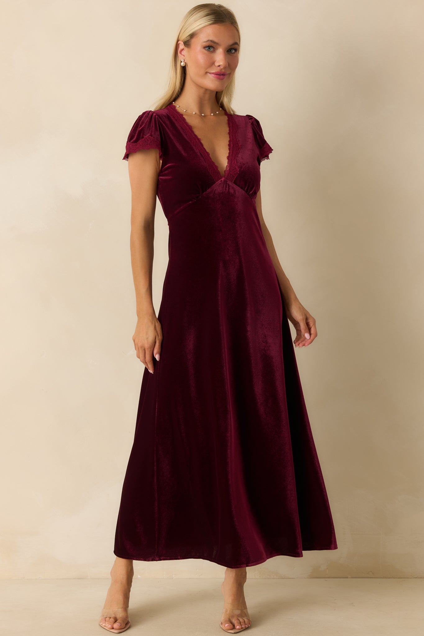 Front view of cranberry velvet dress featuring flutter sleeves, floor-length A-line skirt, and lace-trimmed V-neckline.