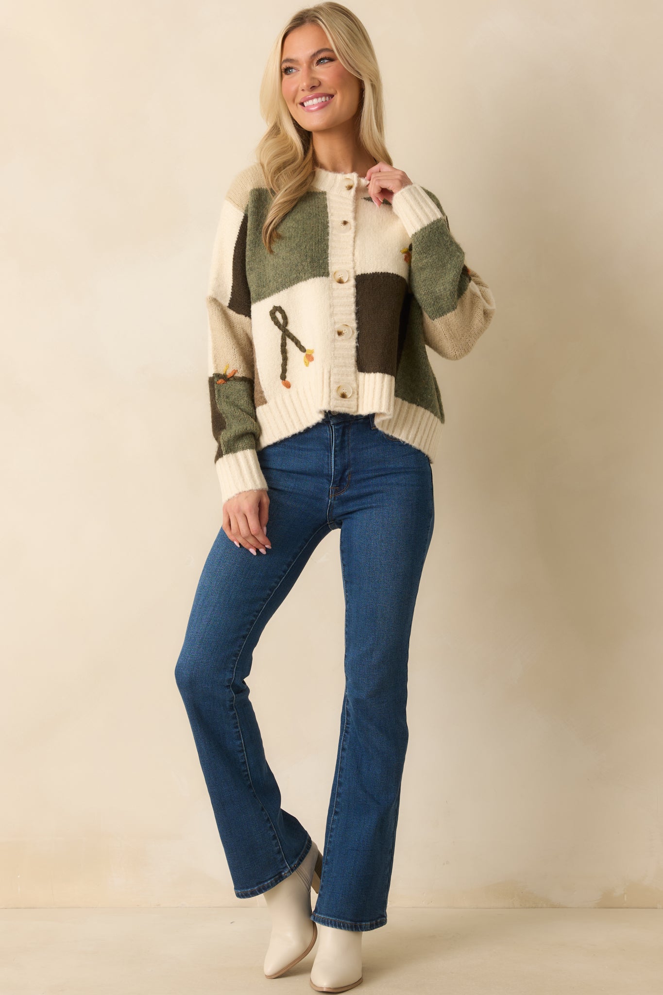 A front view of the ivory knit cardigan featuring an olive and brown colorblock pattern and floral embroidery.