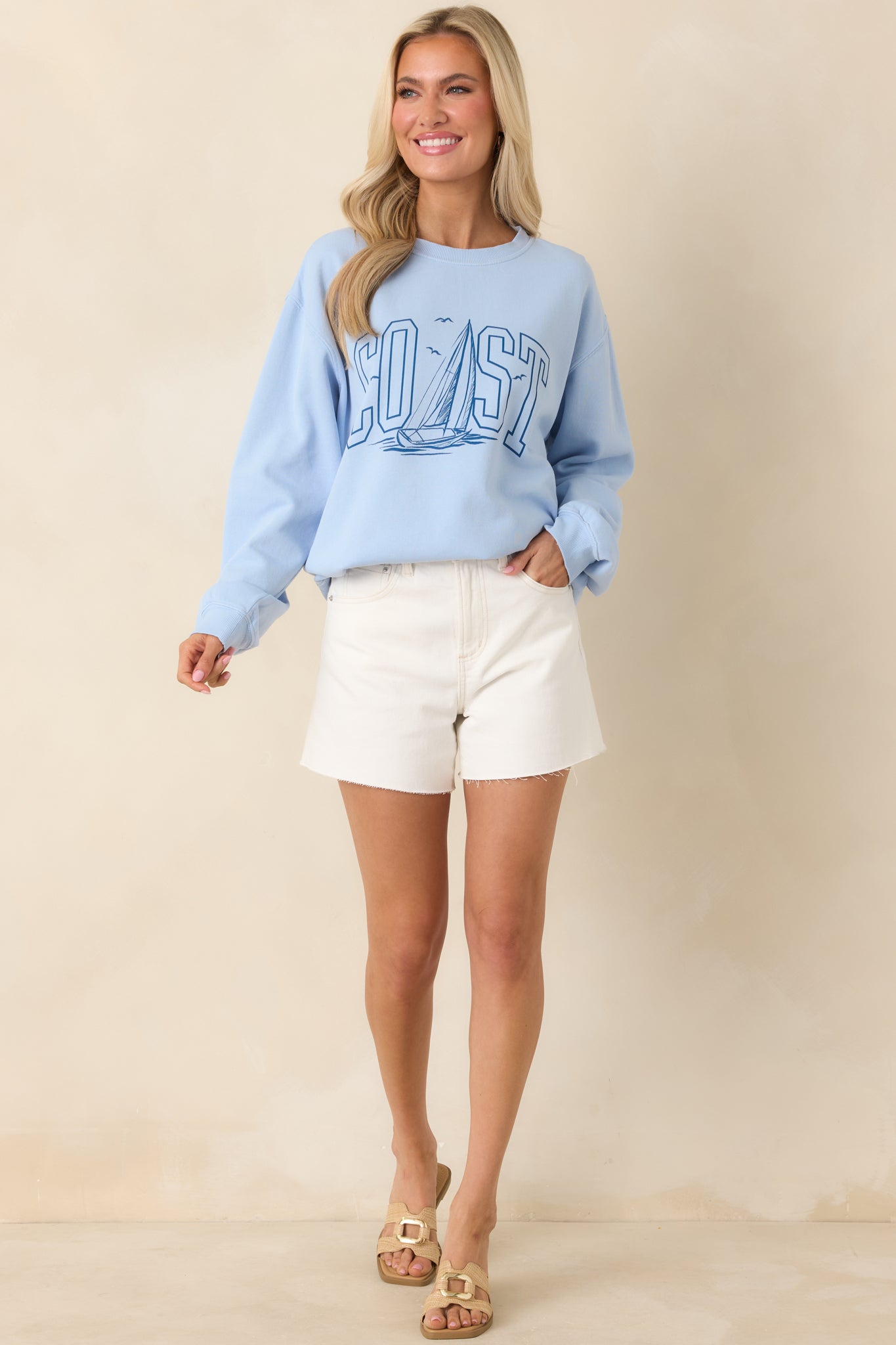 Front view of the light blue sweatshirt featuring a bold “COAST” graphic and sailboat illustration on the chest.