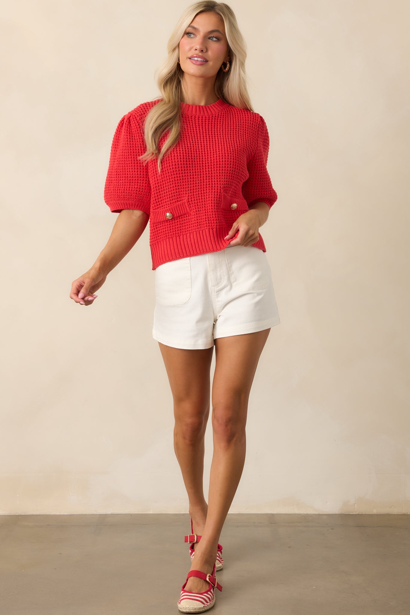 Front-facing view of a red knit top featuring ribbed finishes and gold button embellishments across the chest.
