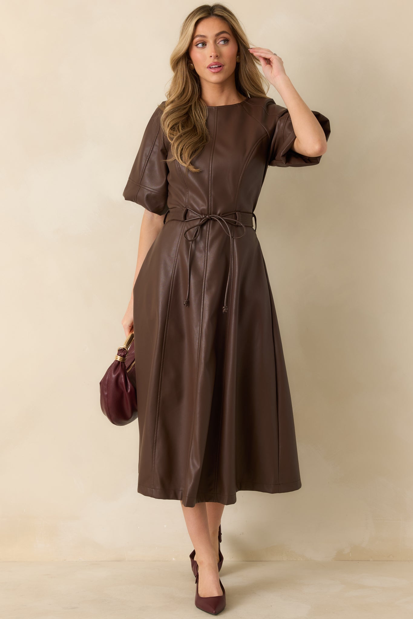 Full front view of brown faux leather midi dress showing short raglan sleeves, crew neckline, and adjustable waist tie.