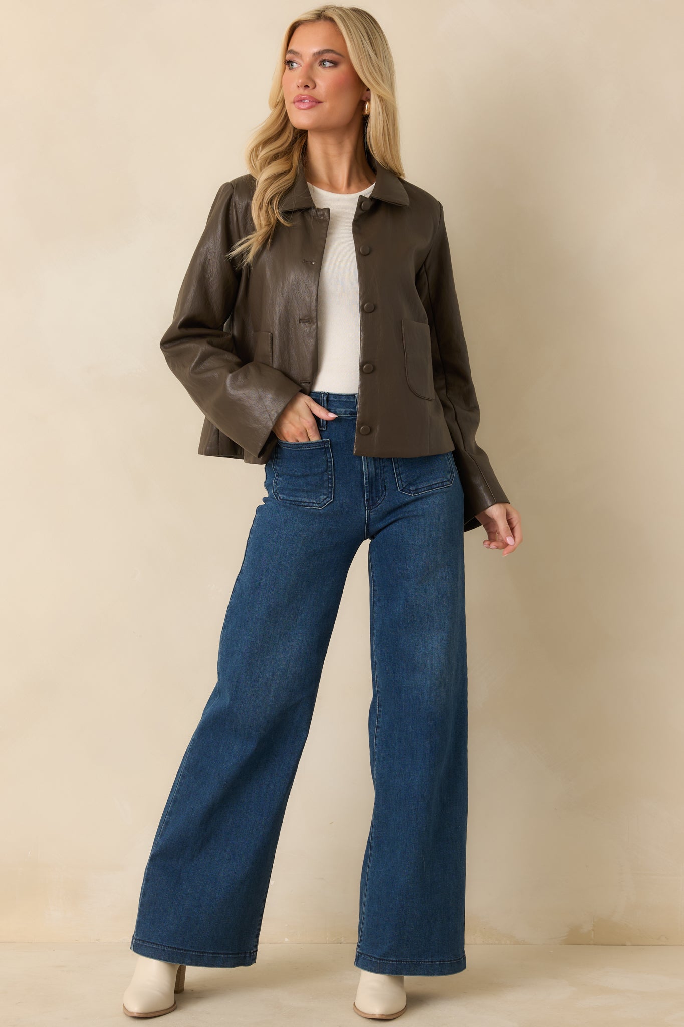 Full front view of dark brown faux leather jacket showing pointed collar, snap button closure, and patch pockets.