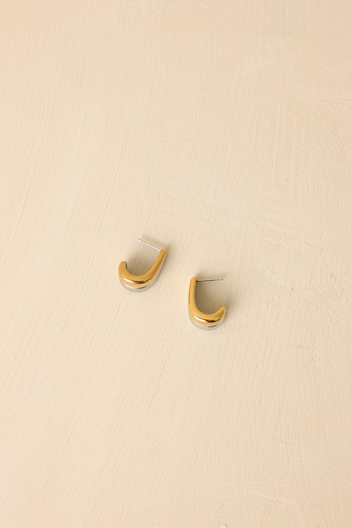 Front view of gold and silver earrings displayed on beige background emphasizing sleek modern design.