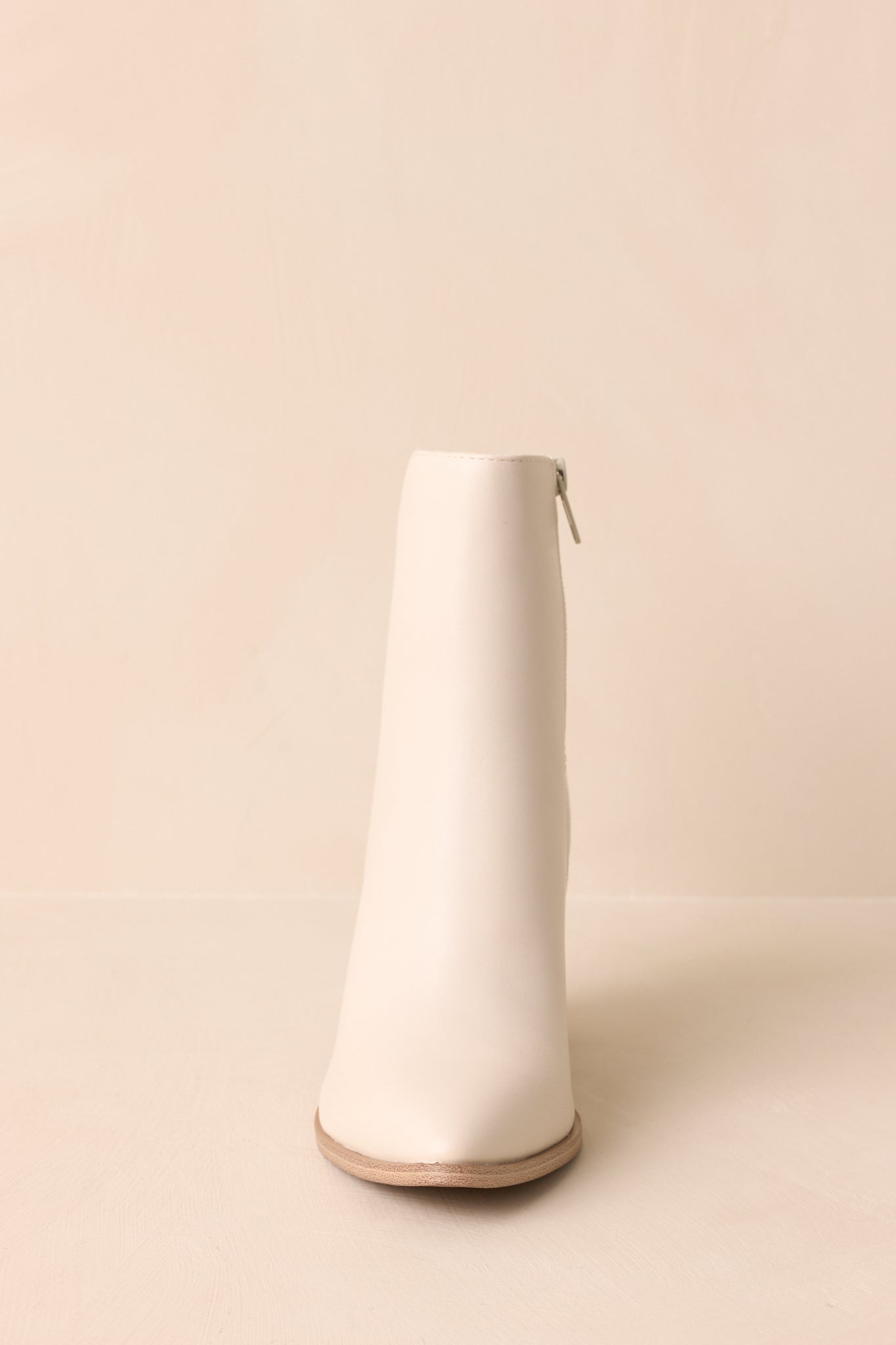 Front view of the ivory ankle boots emphasizing the elongated pointed toe and smooth faux leather construction.