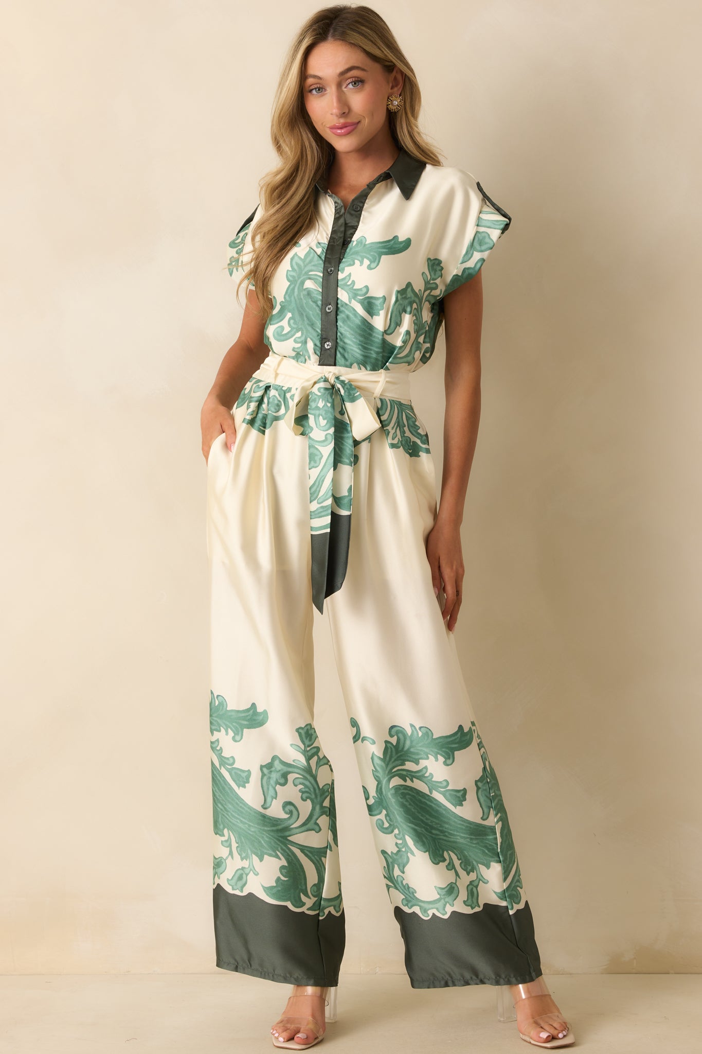 Front view of ivory jumpsuit featuring functional button front, optional self-tie sash belt, and green contrast trim.