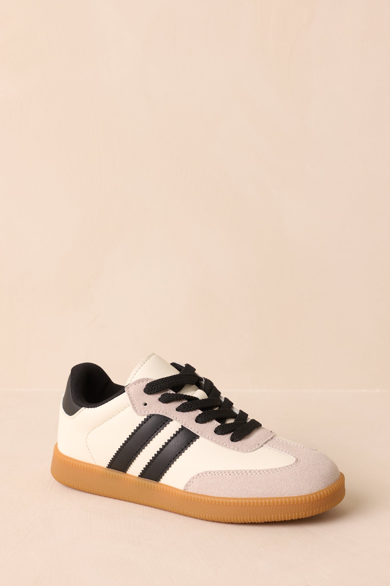 A three-quarter front view of the ivory sneakers showing the rounded toe, contrast black side stripes, and lace-up design.