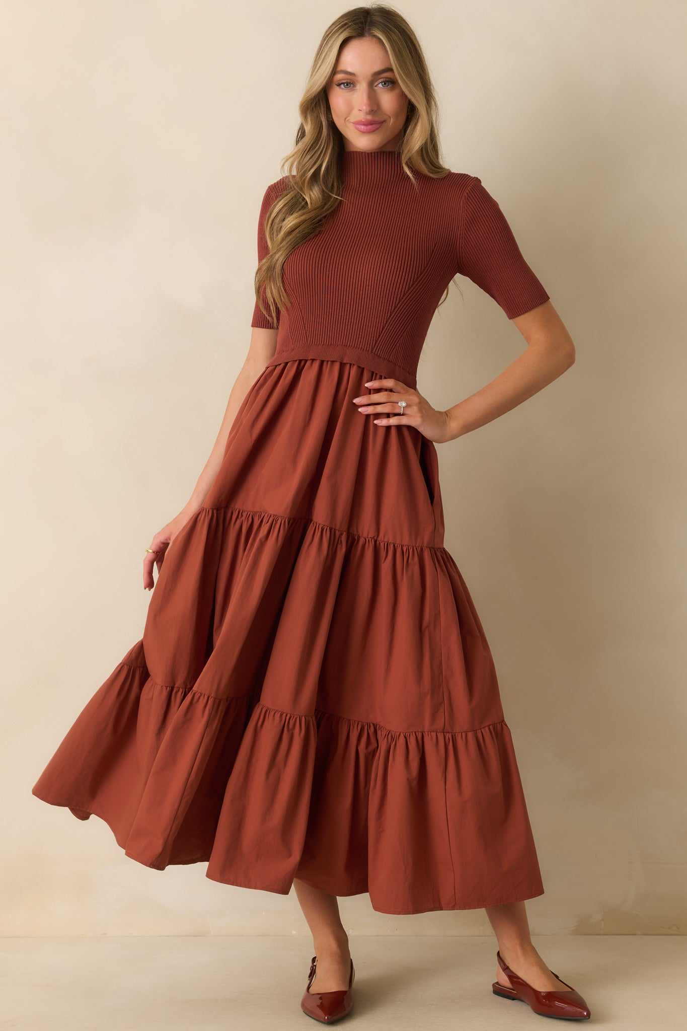 Front view of a rust red maxi dress featuring a defined ruffle-trimmed waist and functional side pockets.