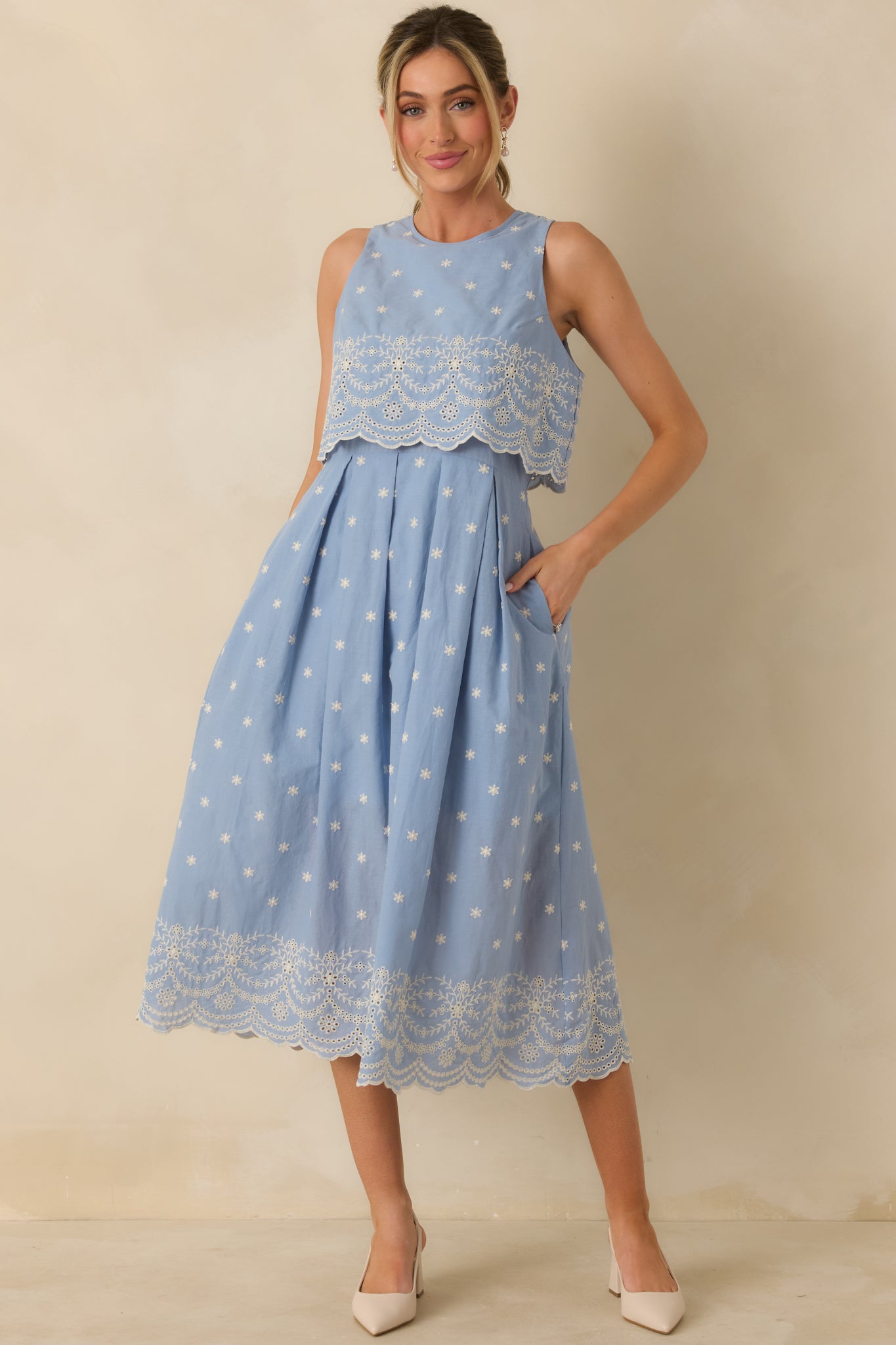 Front-facing view of light blue midi dress showcasing sleeveless bodice, embroidered overlay, and scalloped lace-trimmed skirt.