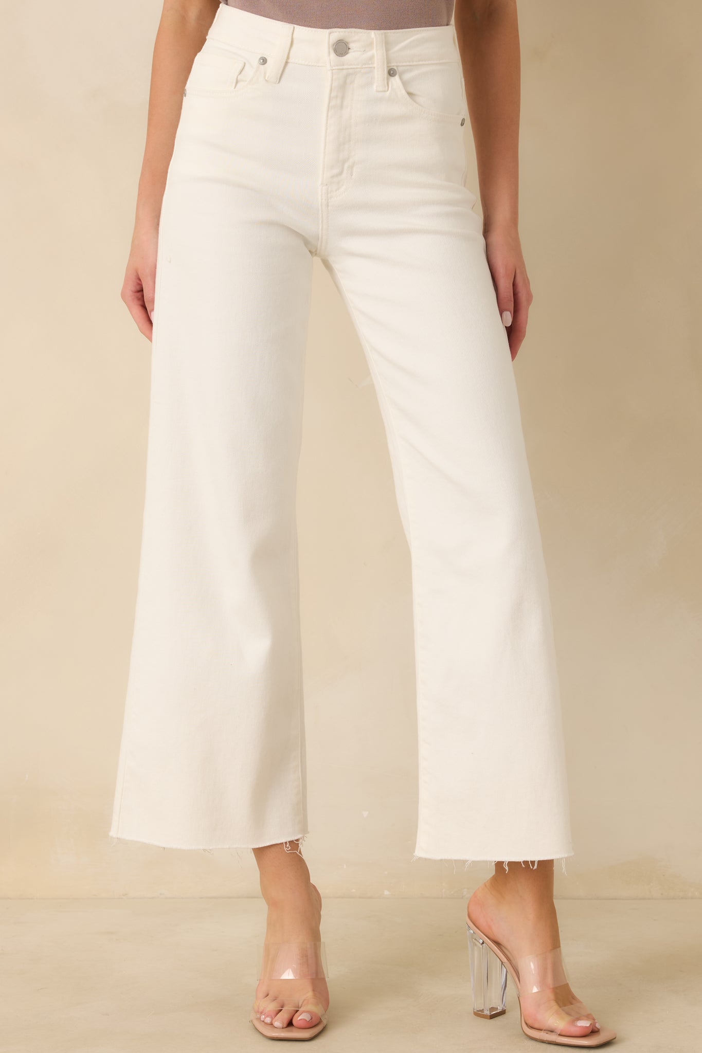 Front waistband detail showing zipper and button closure with belt loops on white denim.