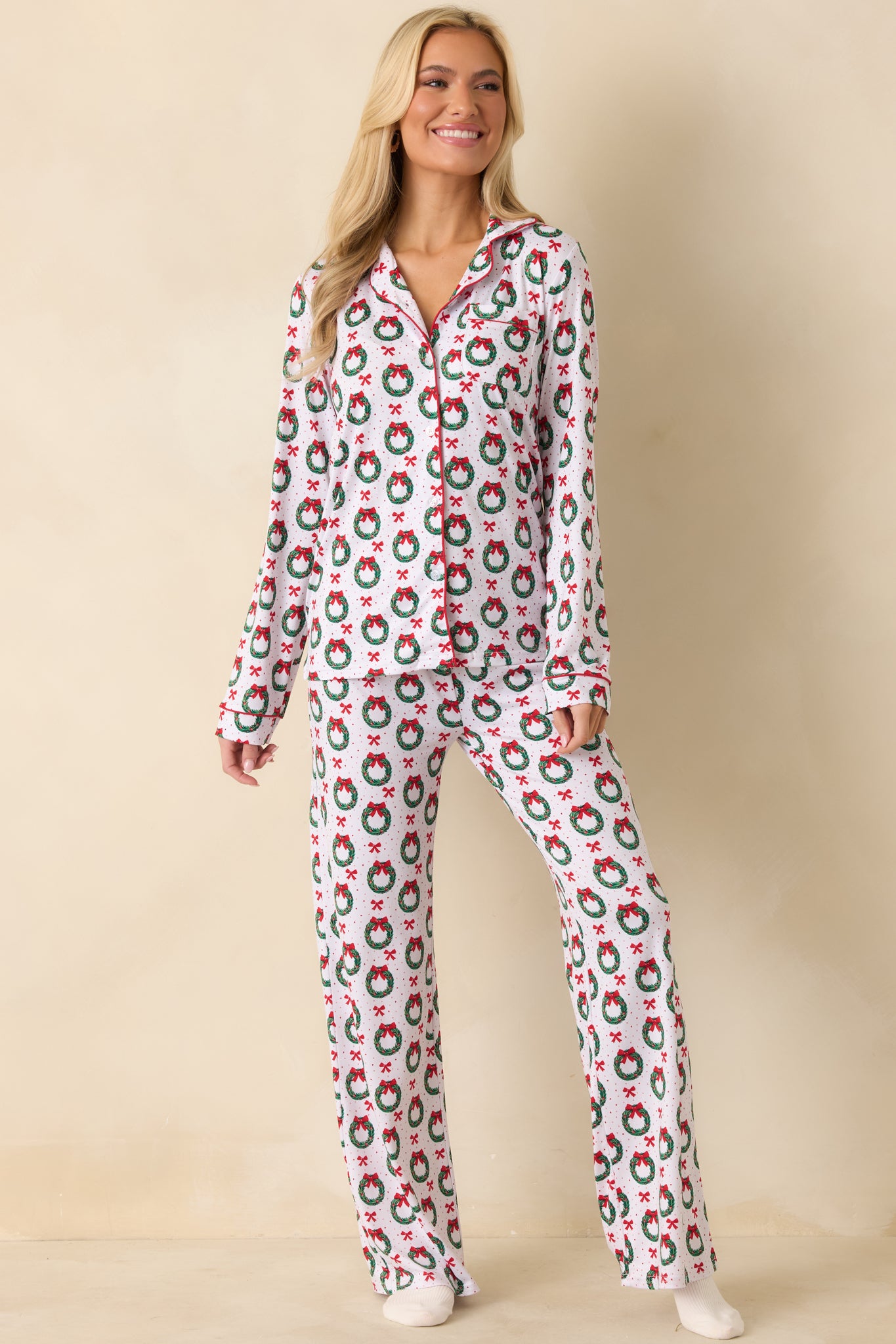 Front view of the white pajama pants showing the allover wreath and bow print with black piping and straight-leg silhouette.