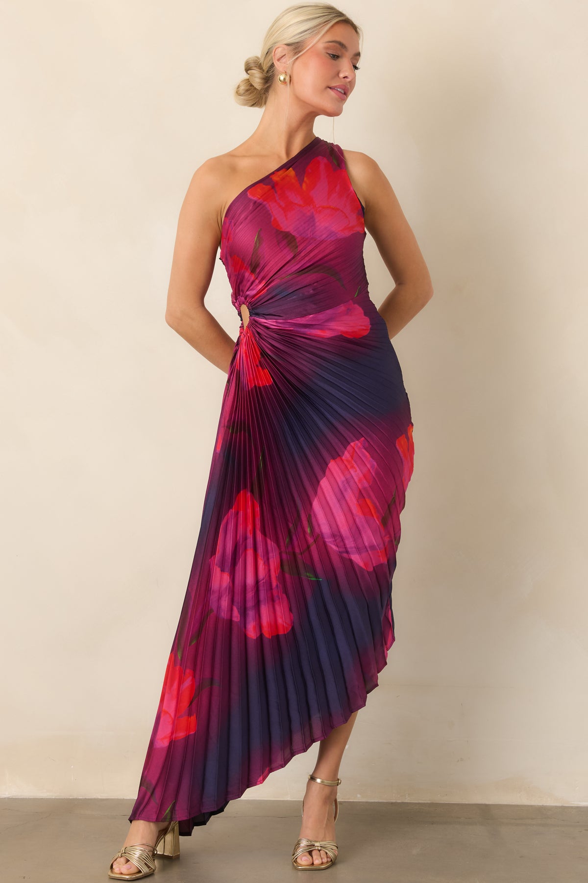 Fuchsia and scarlet floral blooms sweep across the one-shoulder silhouette, ending in a fluid high-low hem.