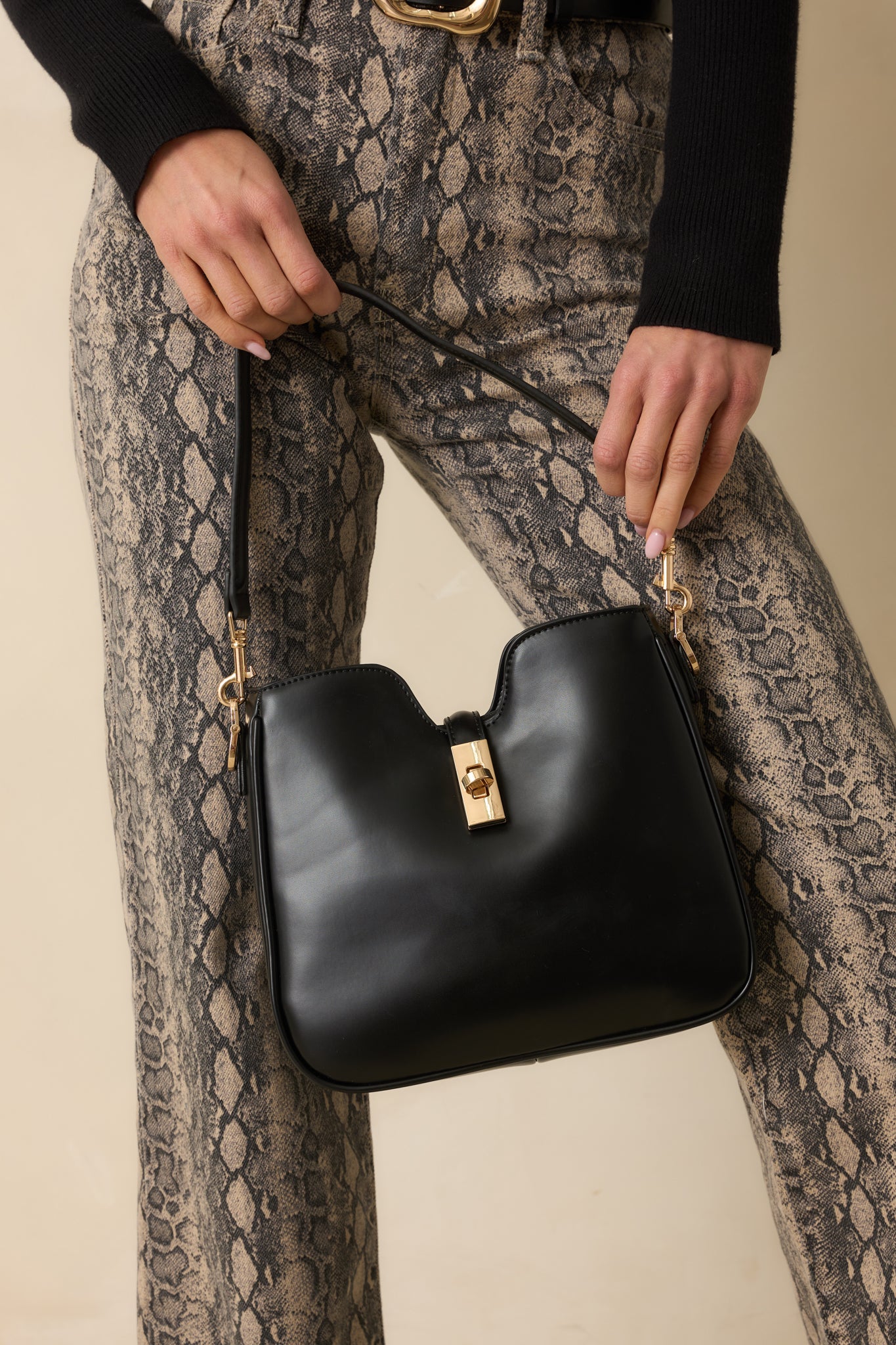 Full body photo showing the structured black faux leather bag with a v-cut top edge and gold turn lock closure.