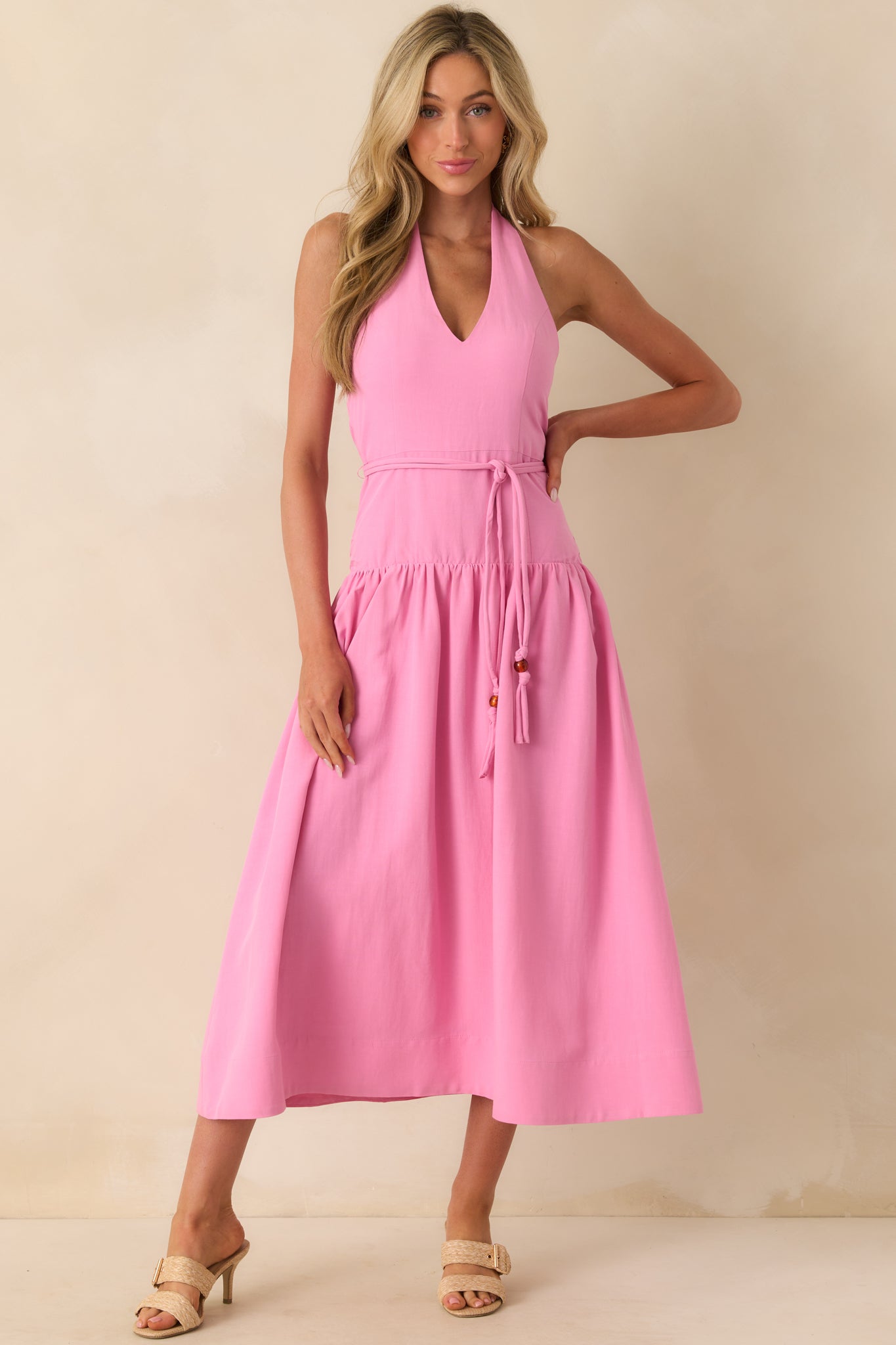 A full body front view showing the pink midi dress with its deep v-neck and halter self-tie neckline.