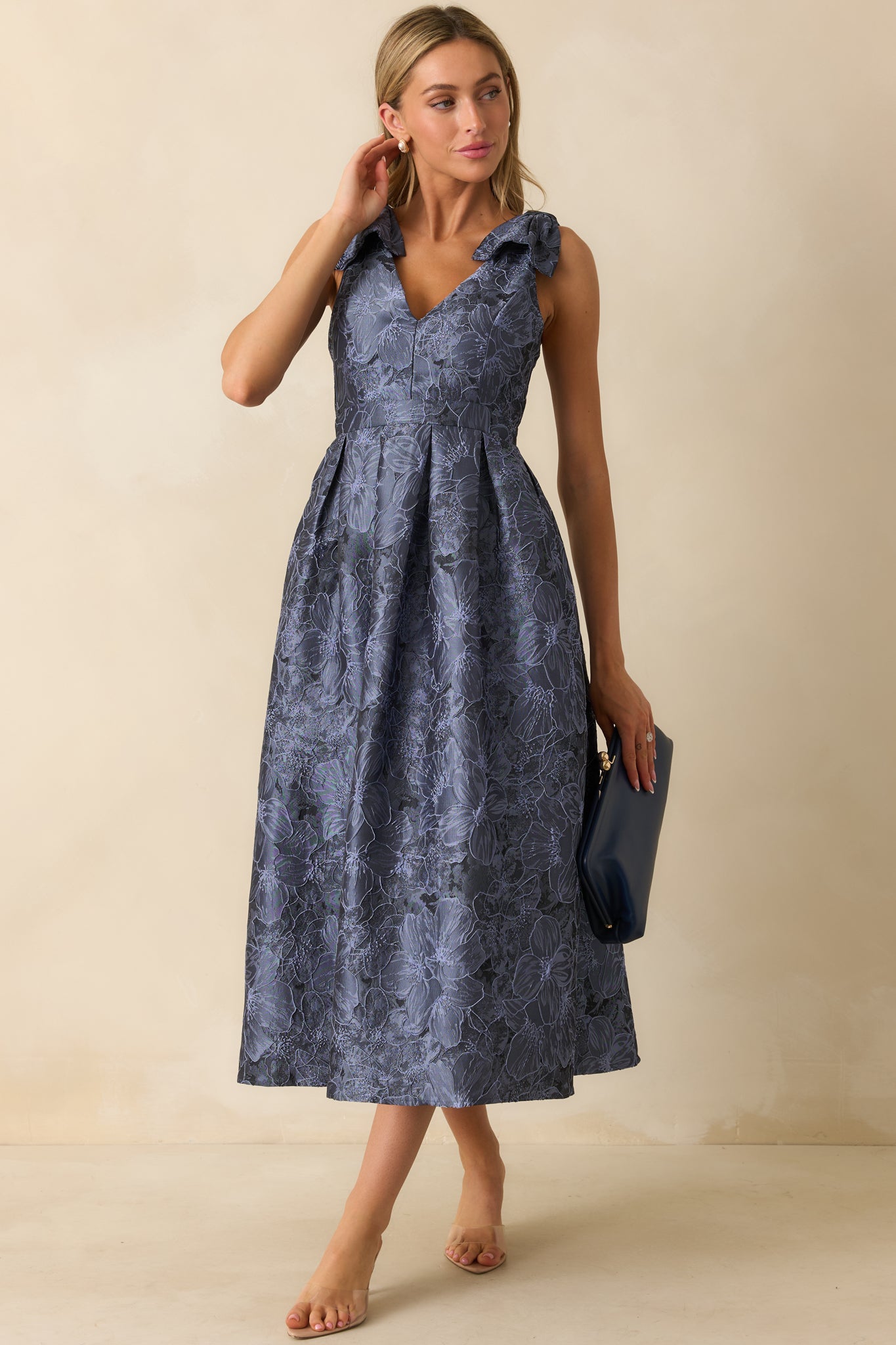 Full-length front view of blue floral midi dress featuring self-tie bow straps, v-neckline, sleeveless cut, and side pockets.