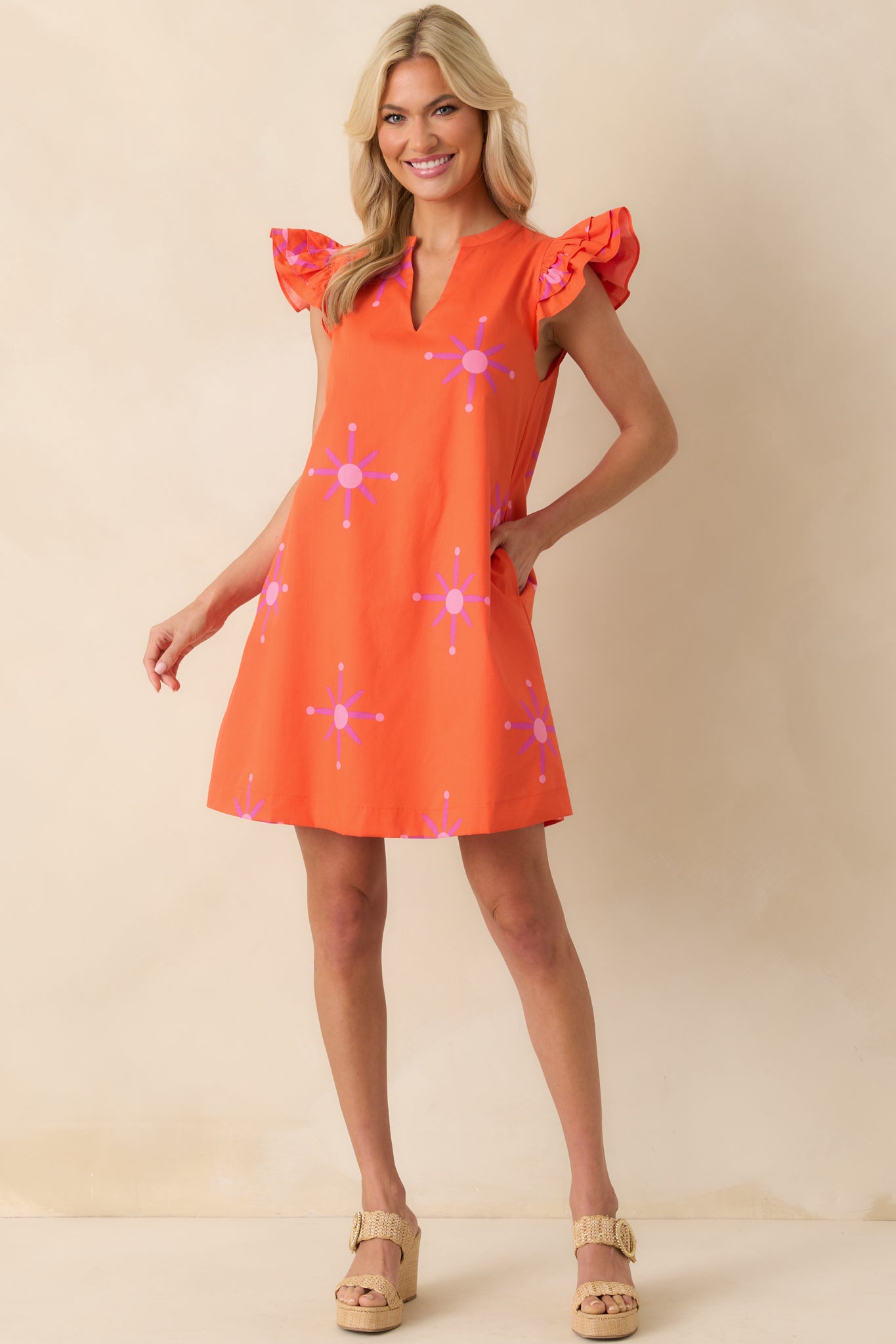 Full body shot emphasizing the layered flutter sleeves and bright orange lining beneath the floral pattern.