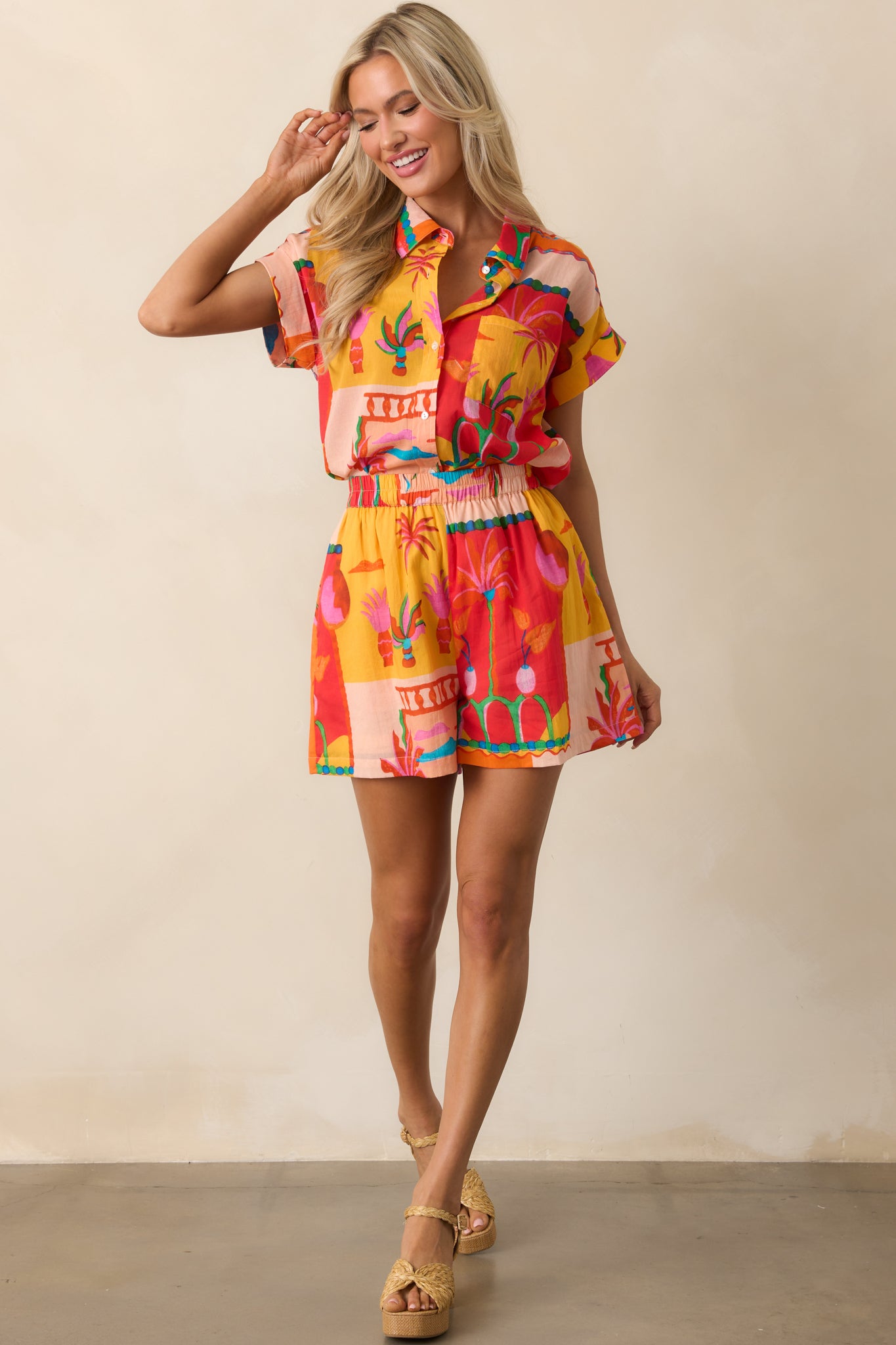 Full body shot showcasing the orange shorts with a vibrant tropical pattern, elastic waistband, and relaxed fit.