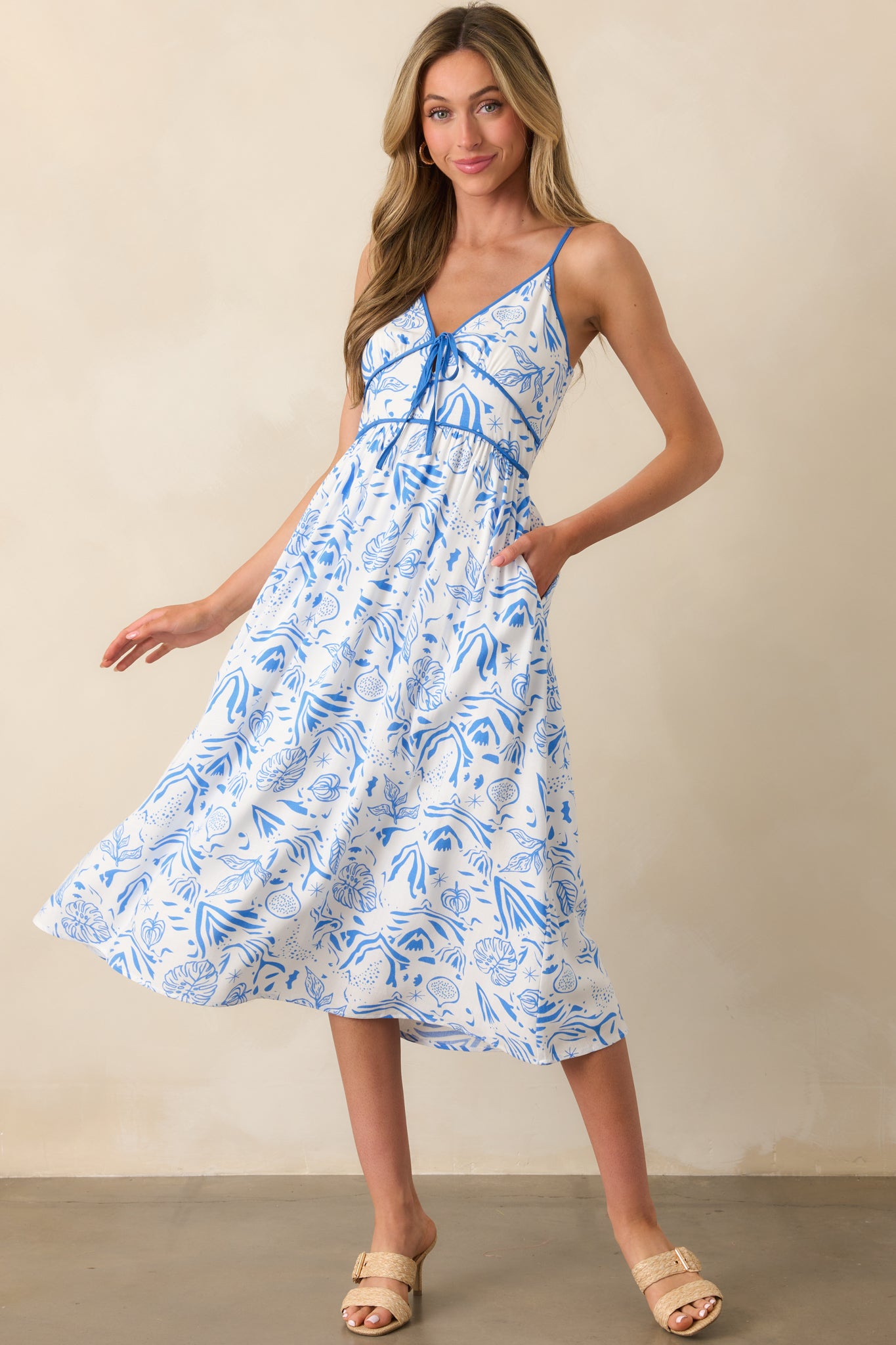 Full view of a midi dress with a blue tropical print, v-neckline, and adjustable spaghetti straps.