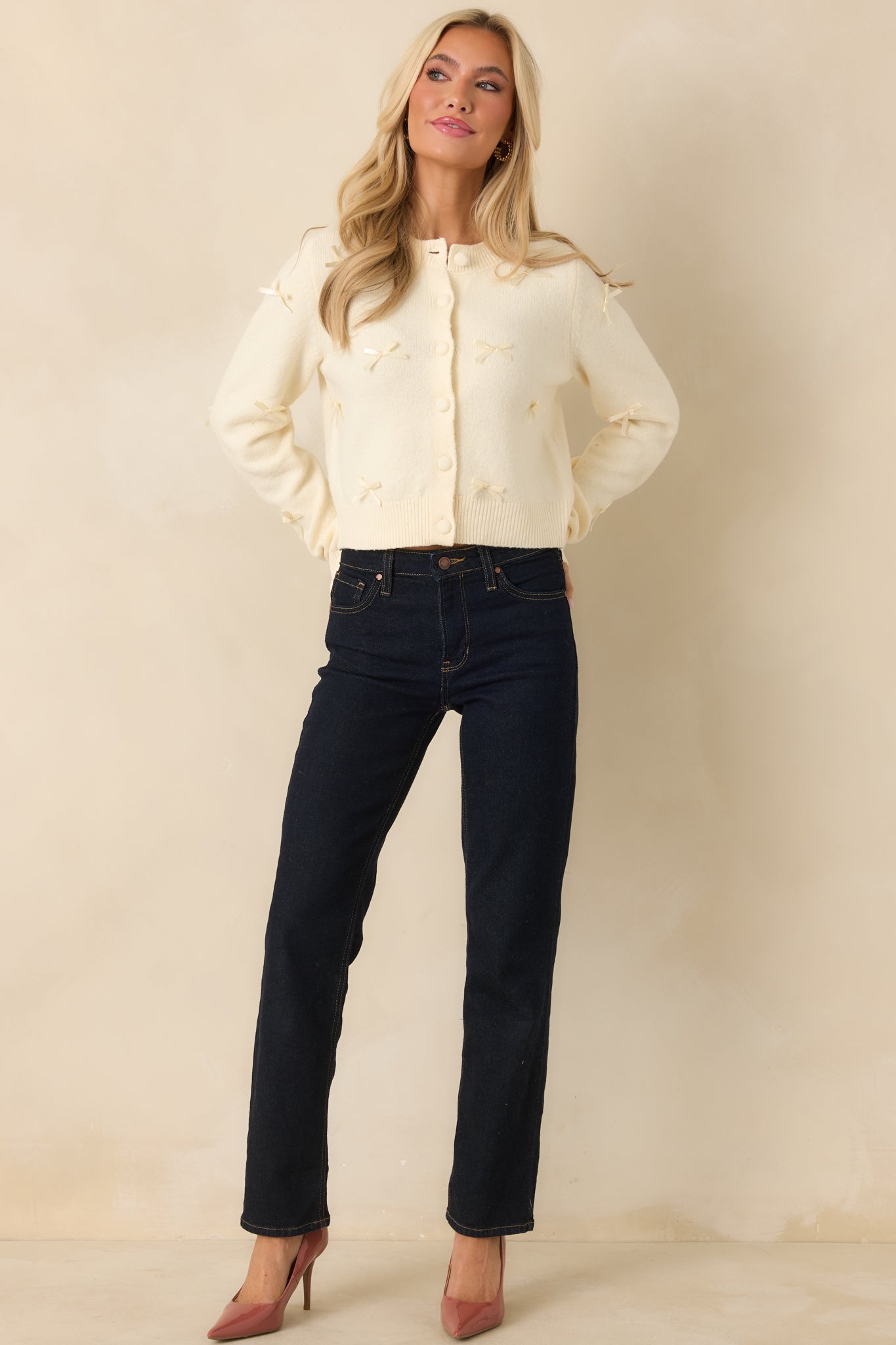 Full view of the cardigan showcasing small bow appliqués throughout the ivory knit fabric.