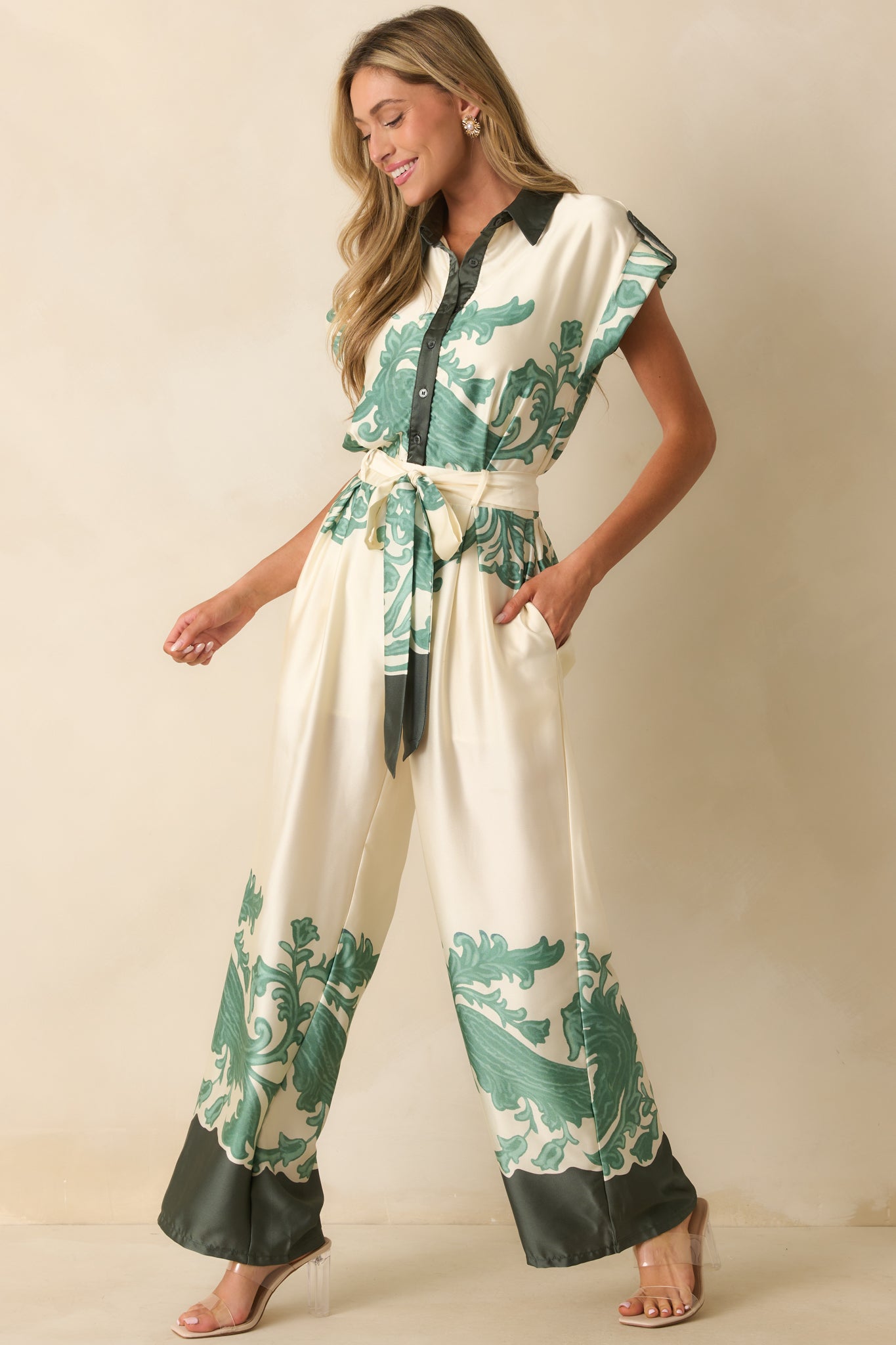 Full-length view of jumpsuit showing collared neckline, cuffed sleeves, and baroque-inspired print along hem.
