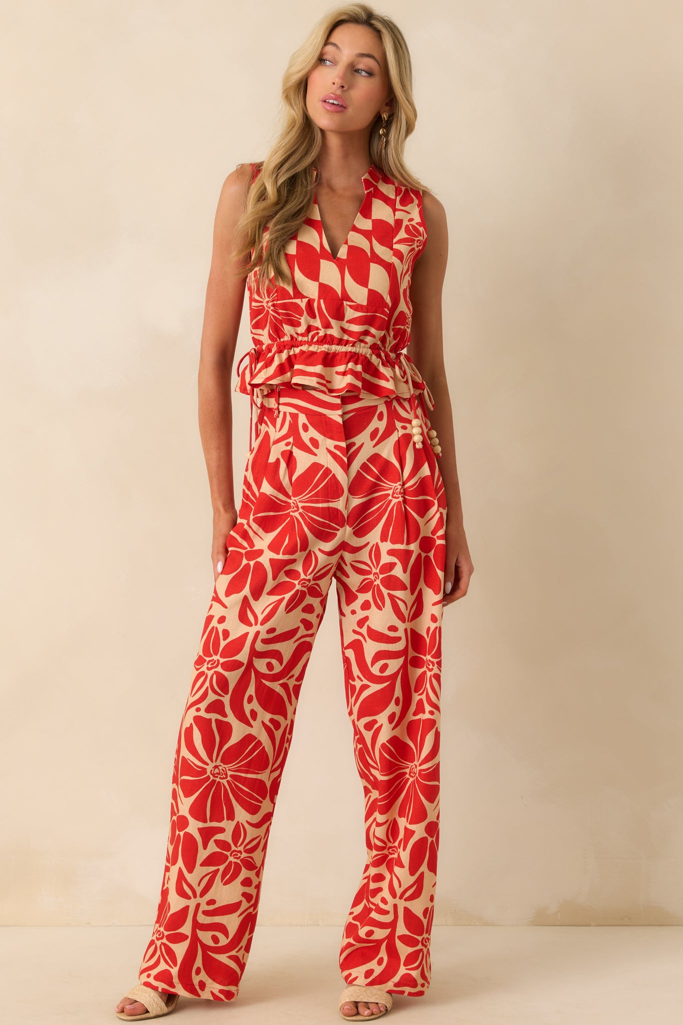 Full body front view of the pants showing the red and beige floral print and wide-leg silhouette.

