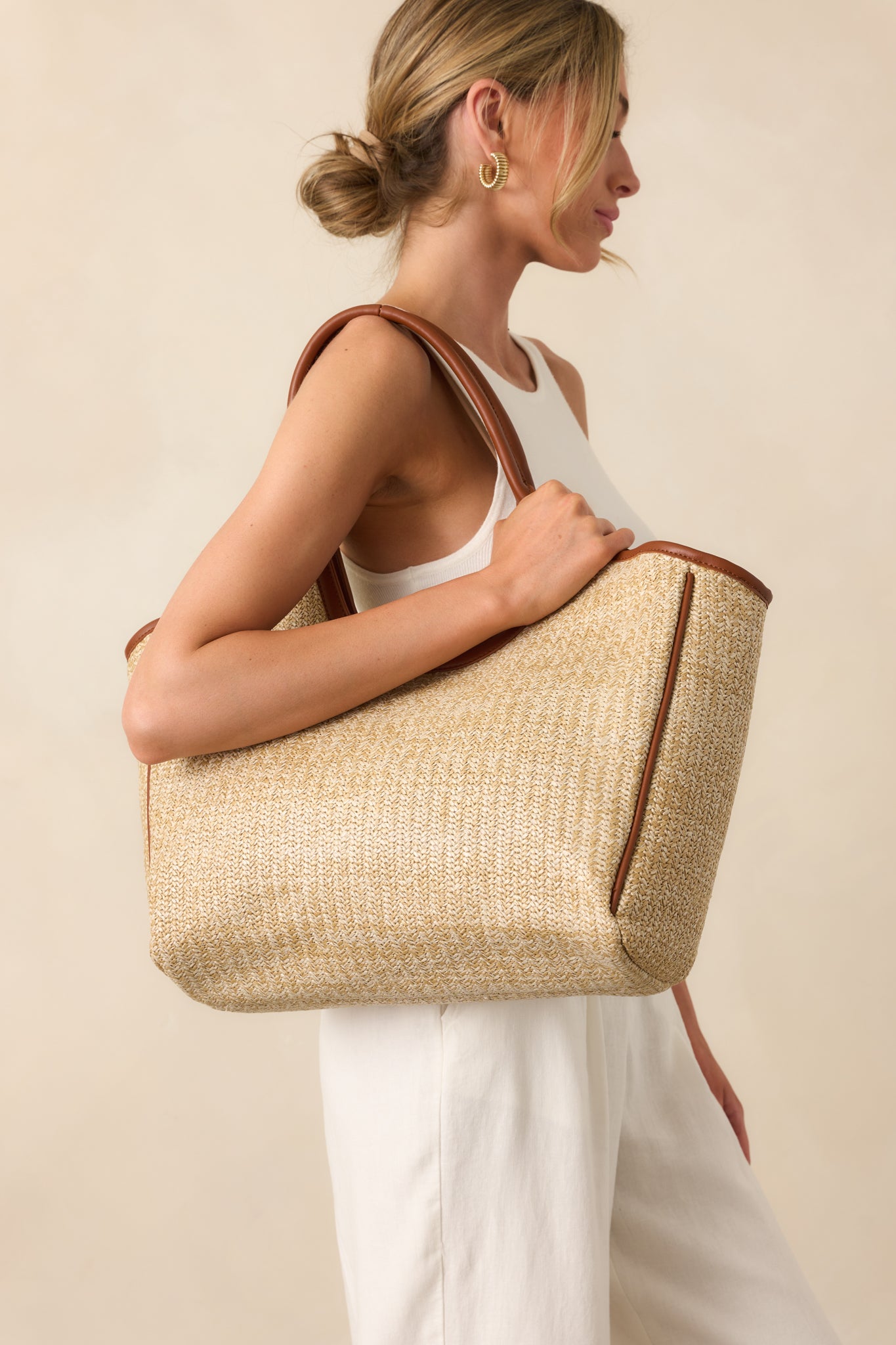 Full view of the natural rattan handbag worn by hand, showing the structured rectangular shape and smooth brown faux leather straps.