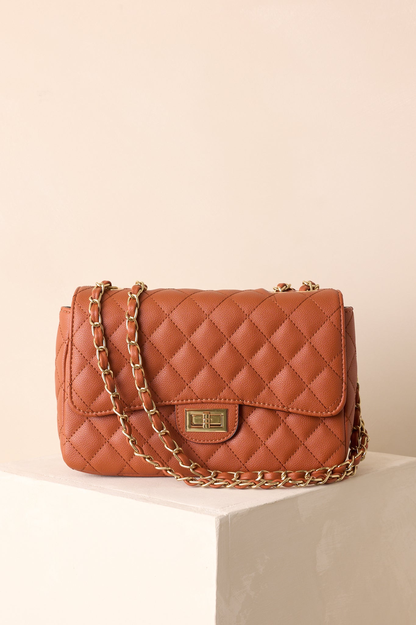Ginger brown quilted handbag with chain strap worn crossbody, showcasing its structured flap design.